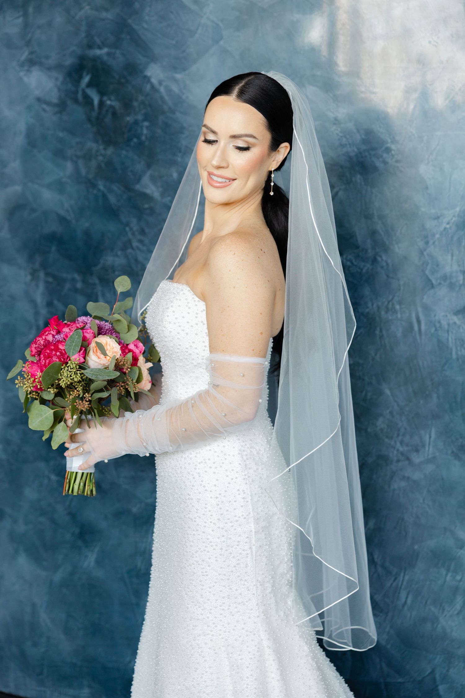 Elegant bridal portrait of a bride in a strapless wedding gown holding a colorful bouquet against a soft backdrop.