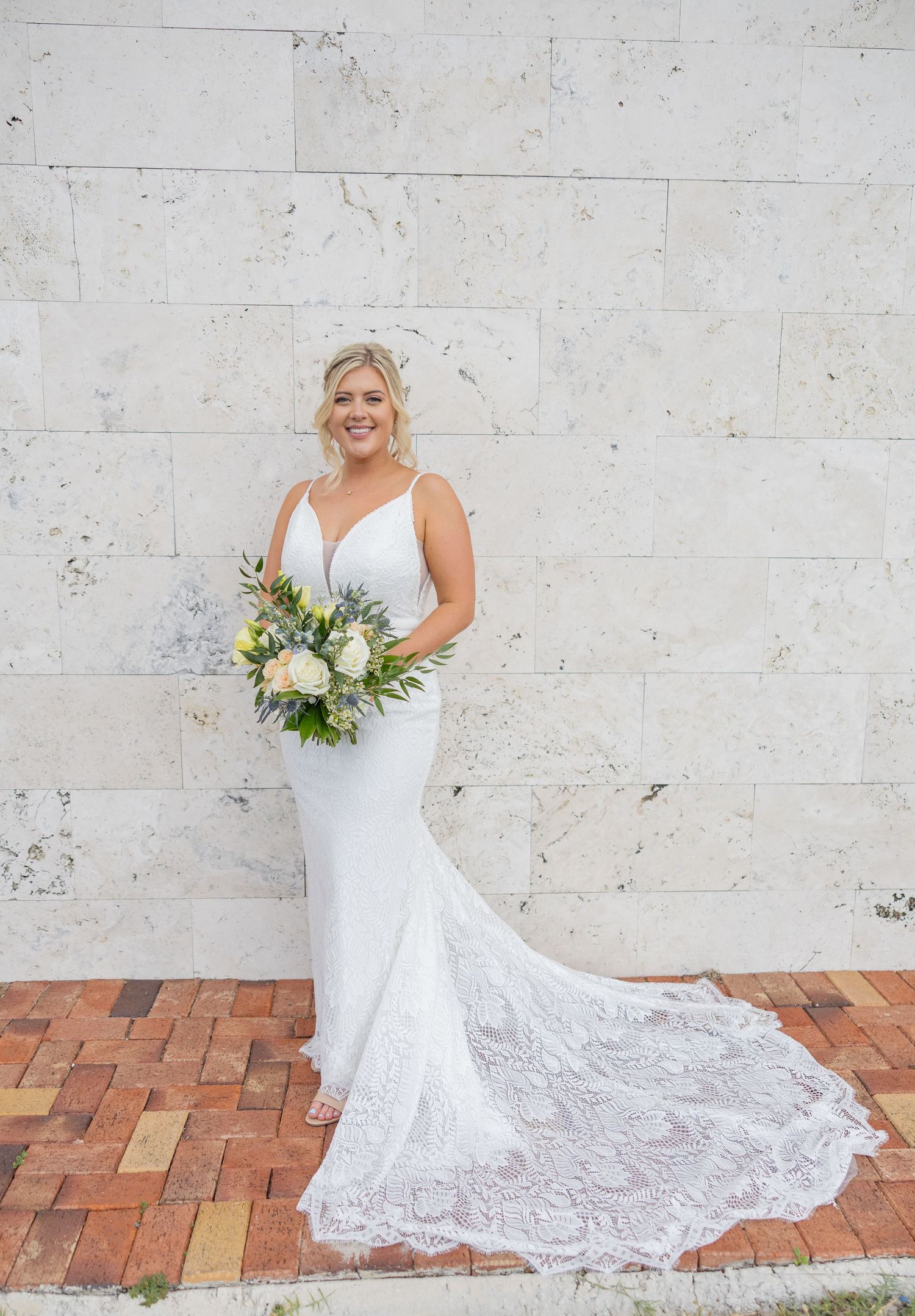 Bride standing alone holding a bouquet during an outdoor wedding portrait session.