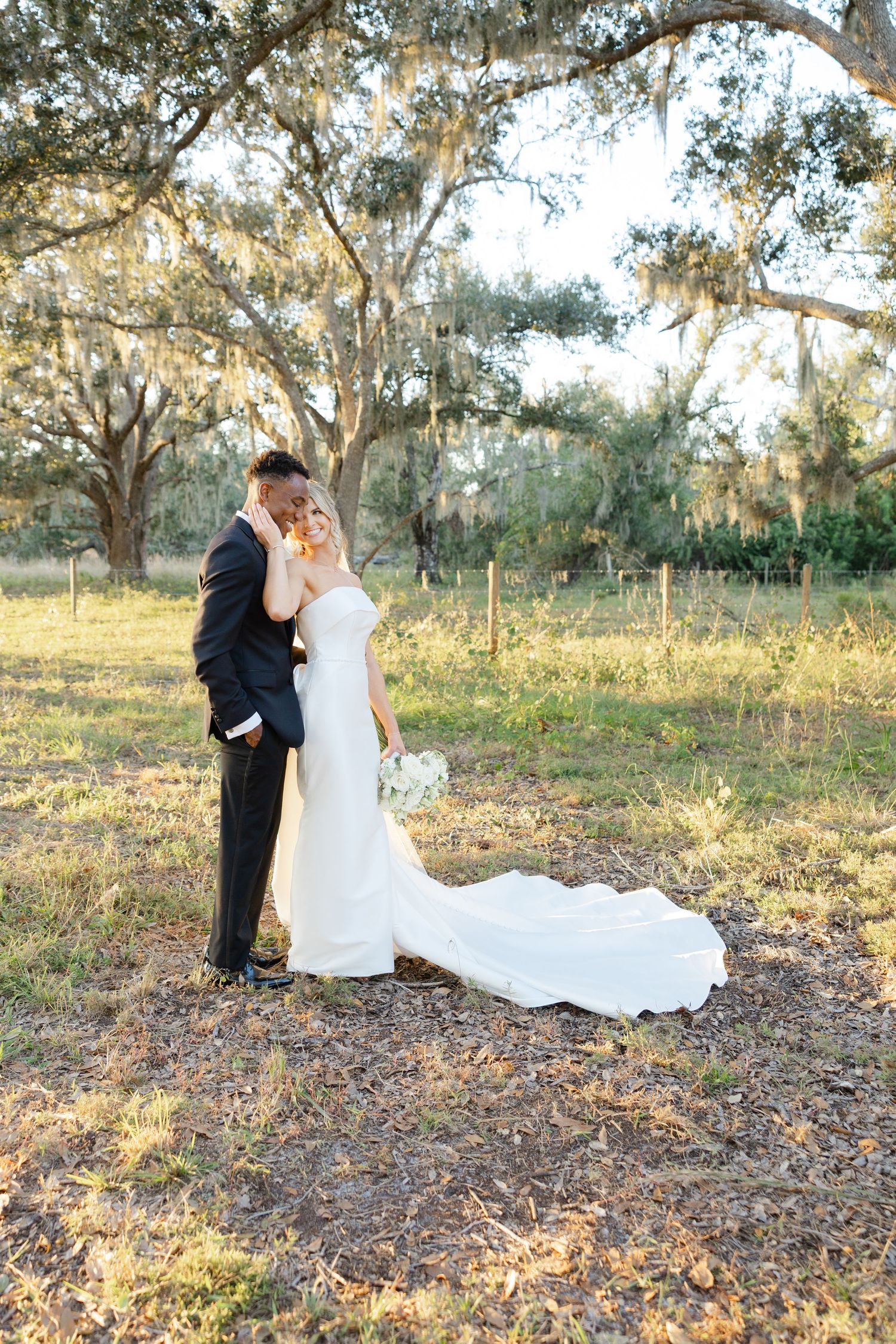 Bride and groom standing together beneath oak trees during an outdoor wedding portrait session.
