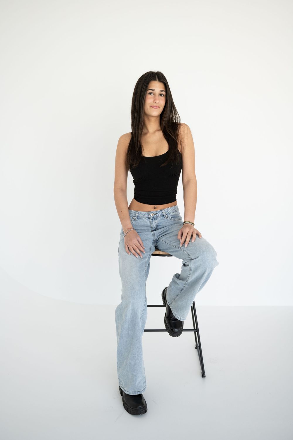 Woman in black crop top and light wash jeans poses against white backdrop in three different seated positions.
