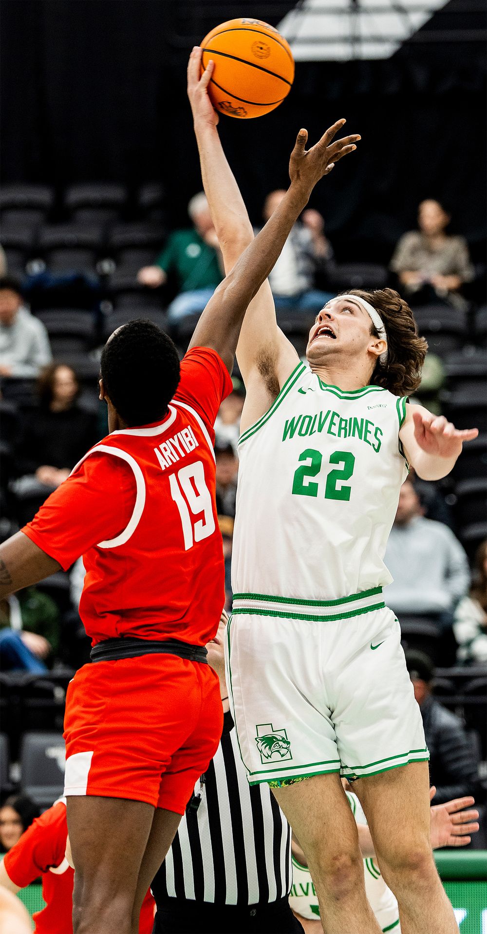 Two basketball players compete for the ball during a game between the Wolverines and their opponents in red uniforms.