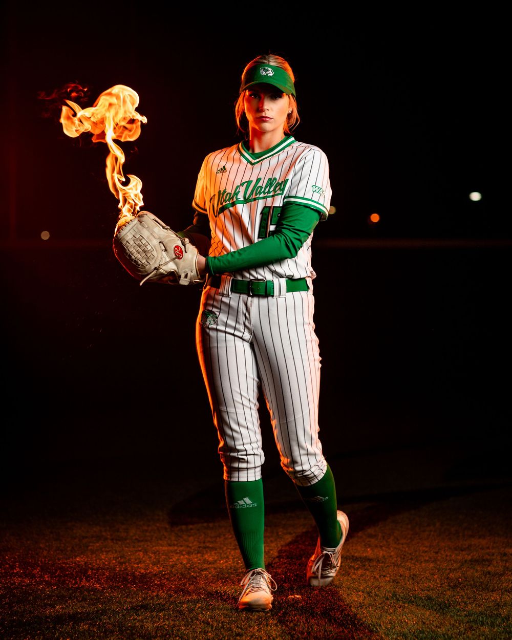 Baseball player in pinstriped uniform holds a flaming glove while posing dramatically on dark field at night.