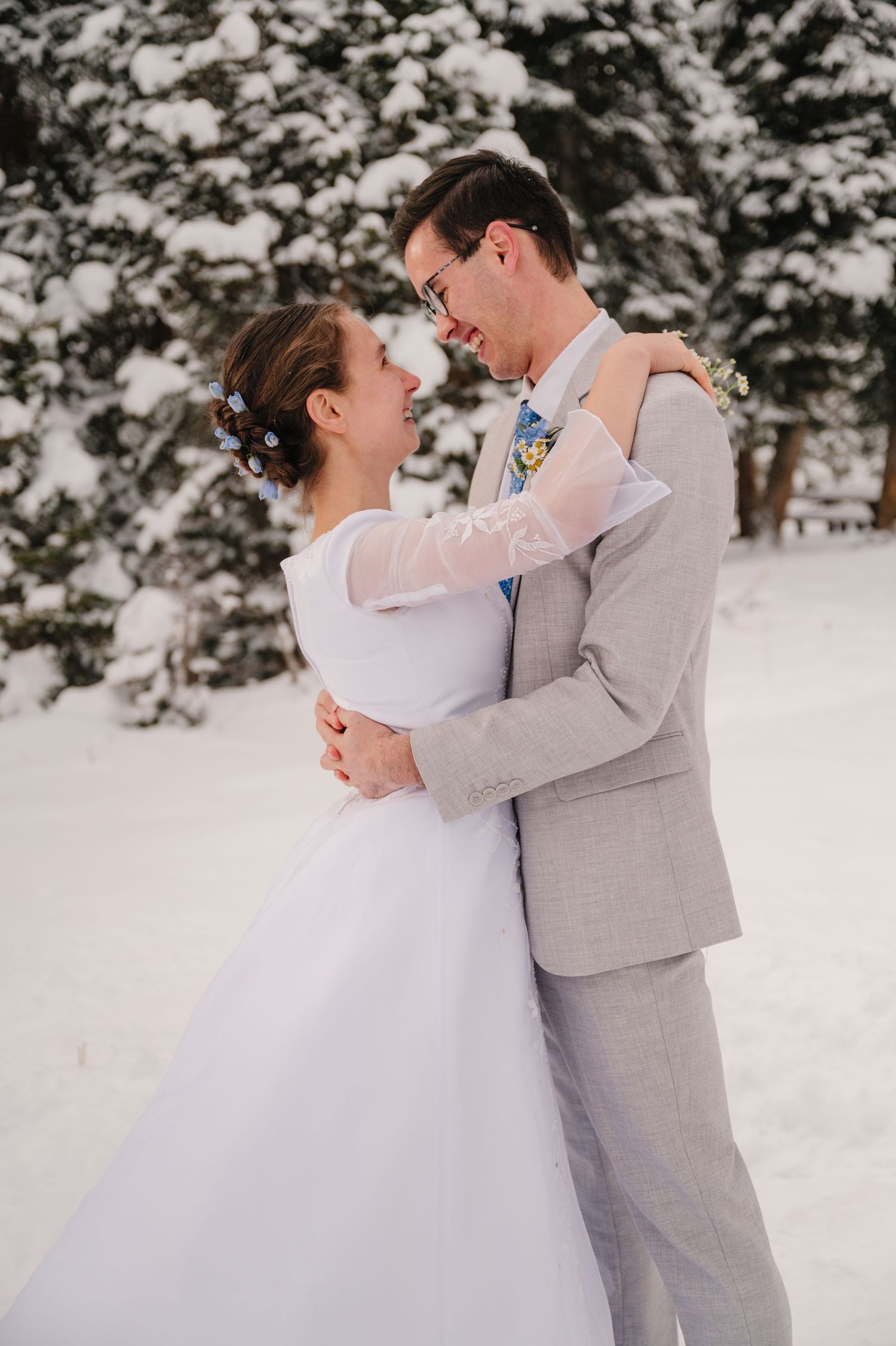 A winter wedding portrait with snow-covered evergreens in the background.