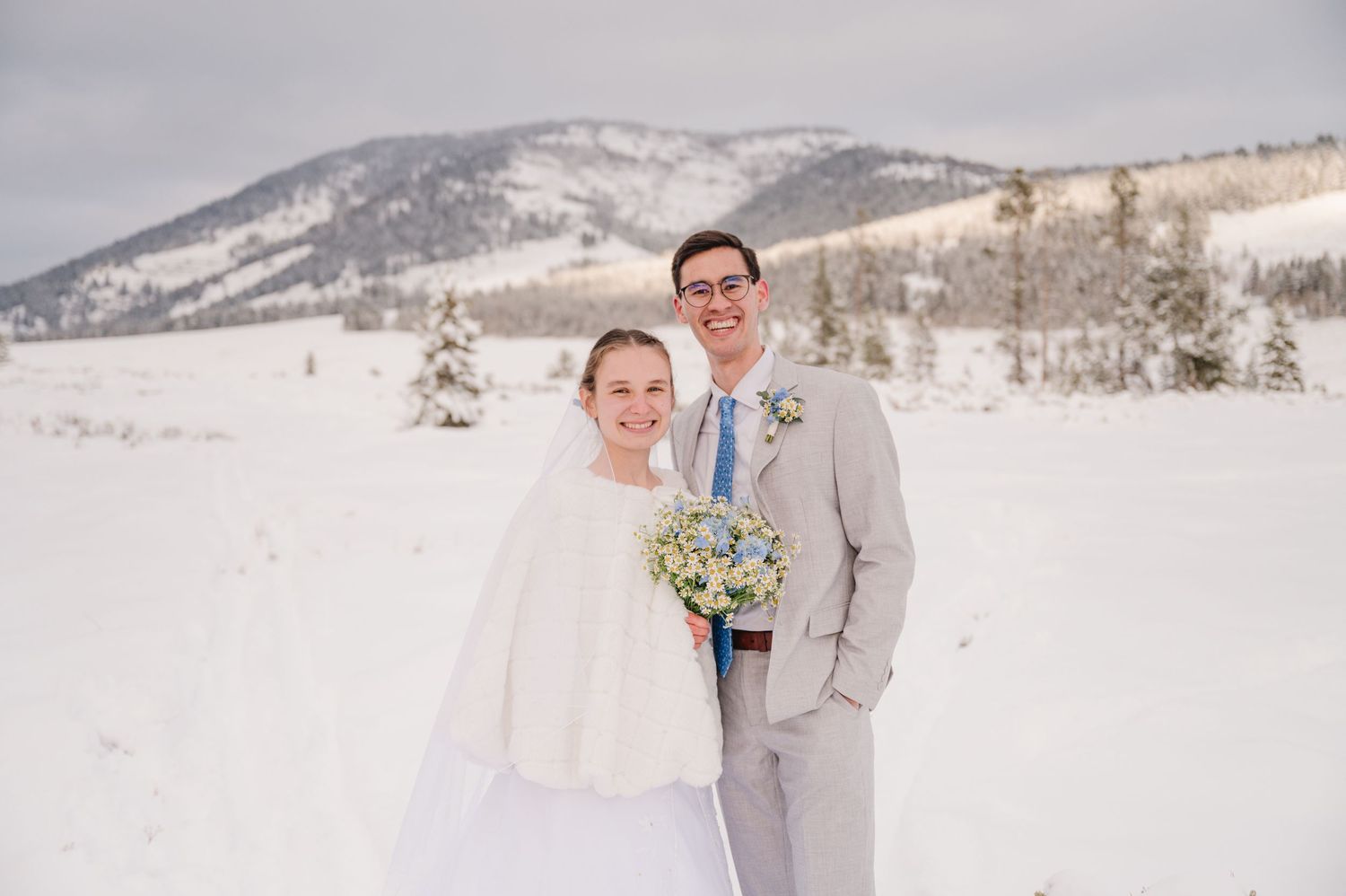 A winter wedding couple poses in front of snow-covered mountains.