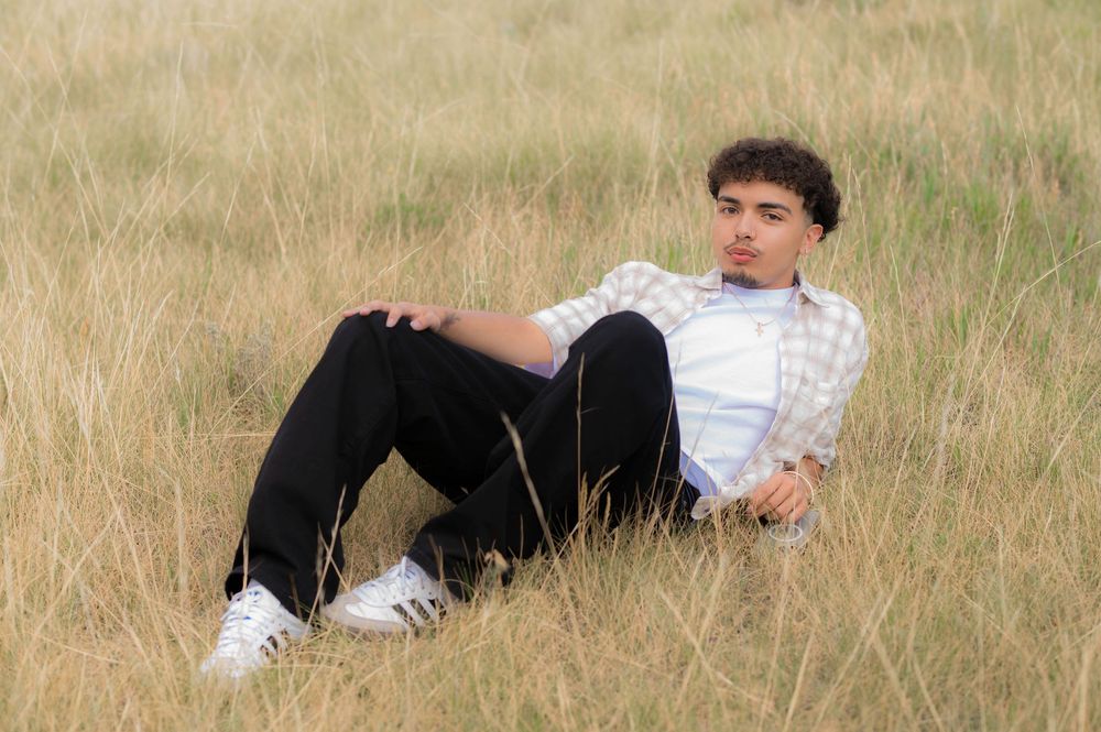 Young man in plaid shirt and black pants relaxing in a golden grass field on a sunny day.