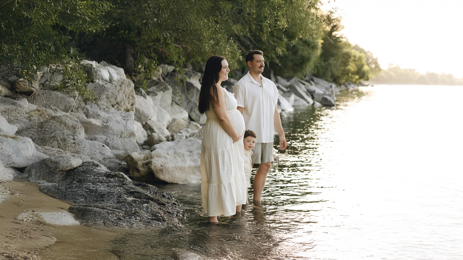 A family shares an intimate moment together in a sunlit park with trees in the background during golden hour.