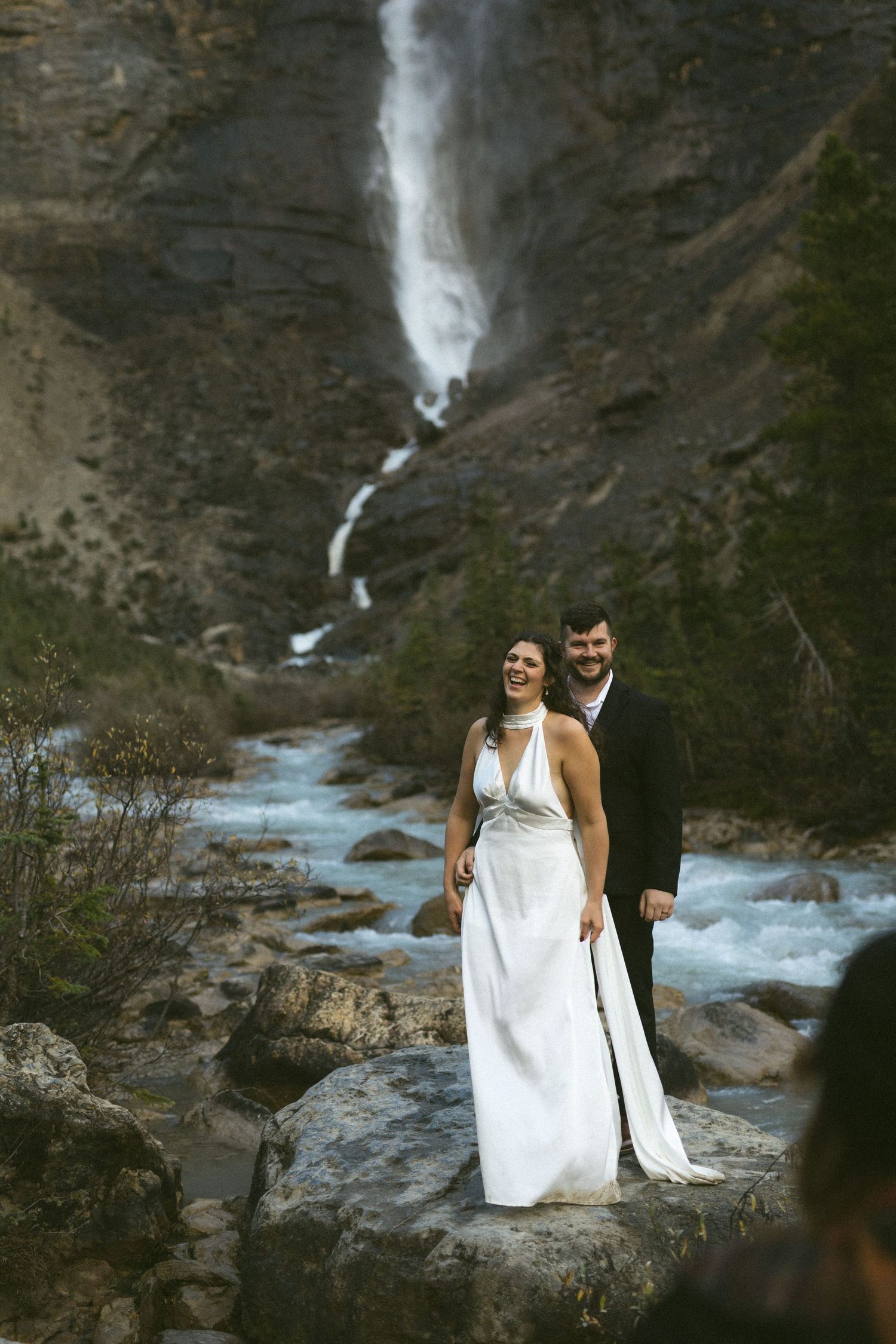 Bride and groom laugh beside a waterfall during their Yoho National Park elopement