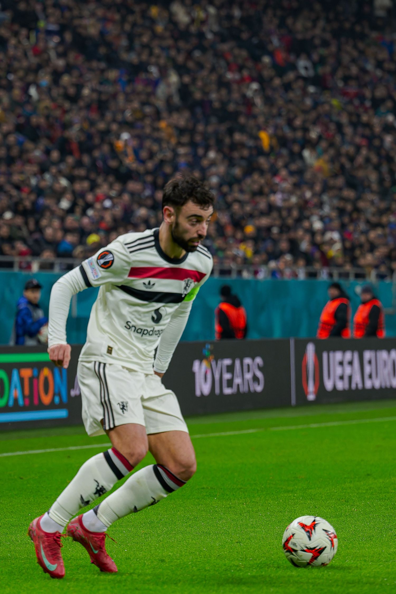 Soccer player in white uniform dribbles ball during UEFA Europa League match at stadium.