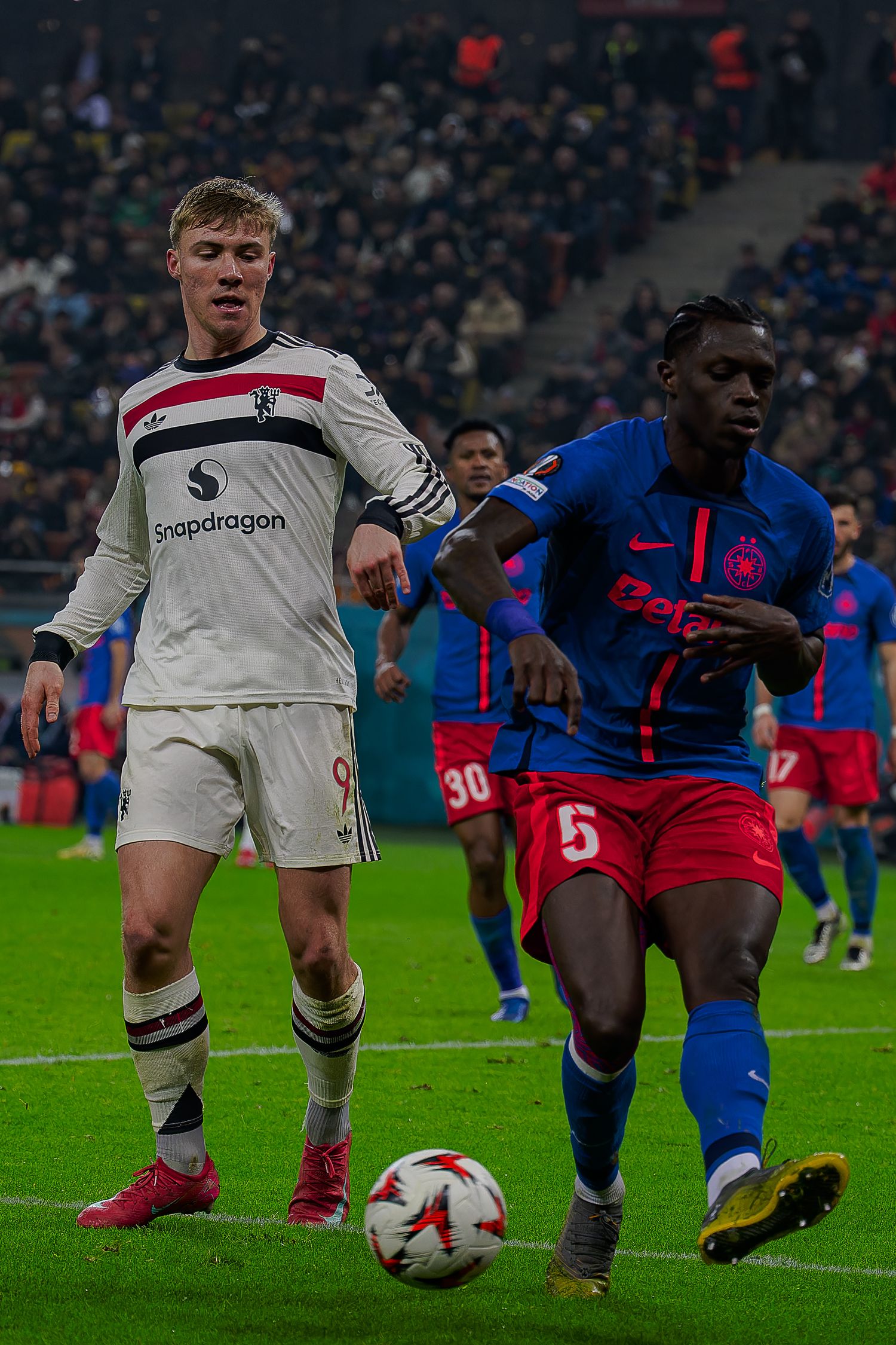 Soccer players from DC United and Atletico Madrid compete for the ball during a match at a crowded stadium.