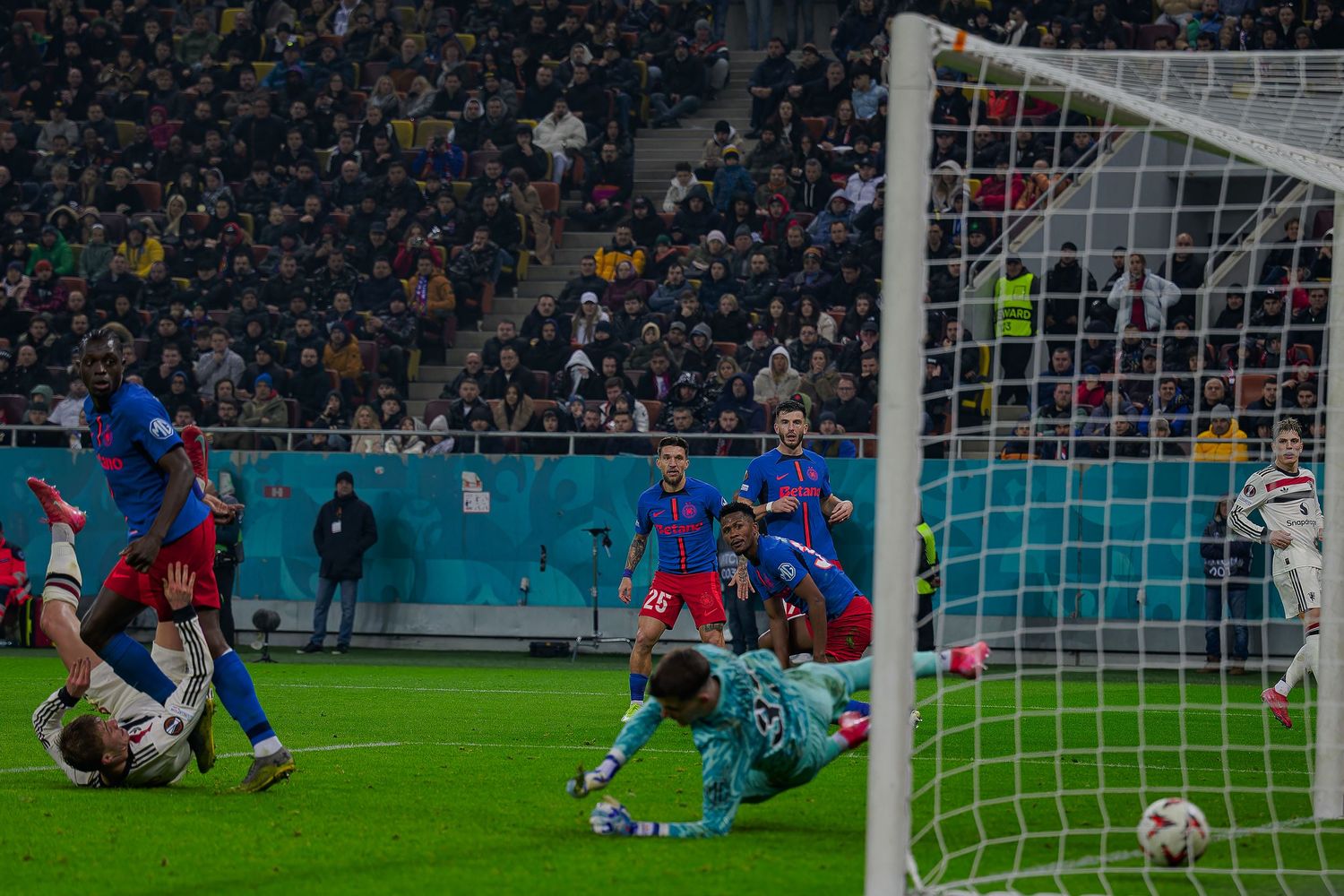 Soccer players scramble for the ball near the goal during an intense match at a stadium.