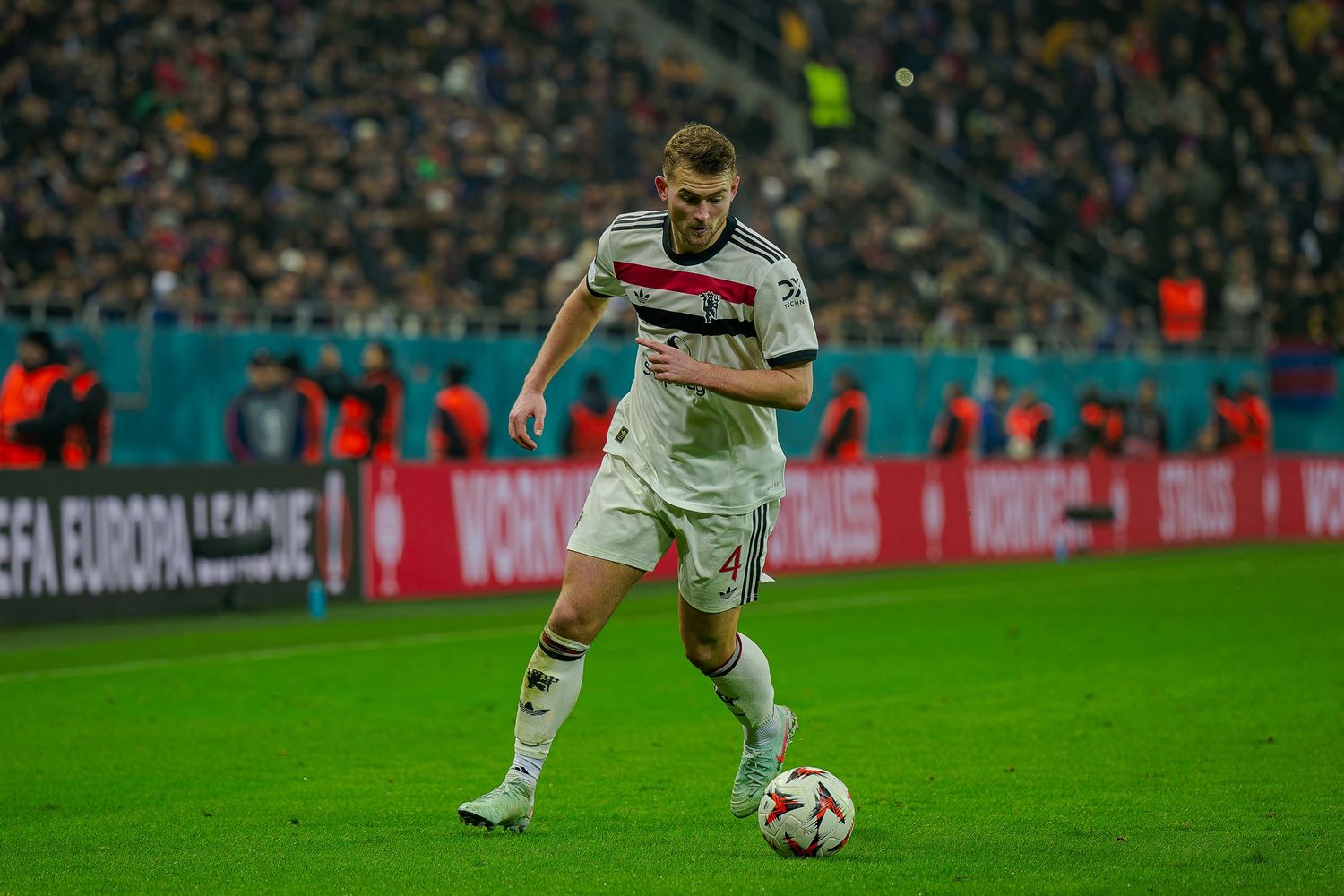 Soccer player in white jersey with red stripe controls the ball during Europa League match.