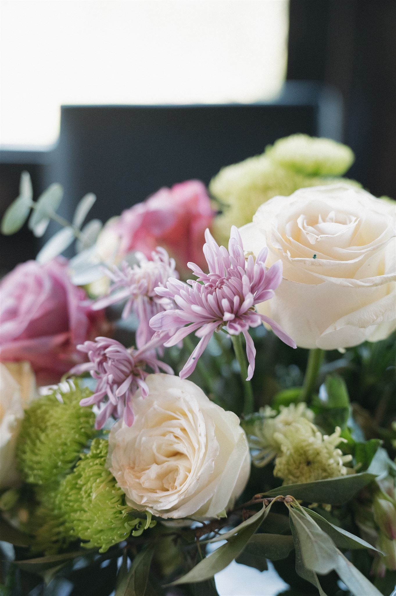 Elegant floral arrangement featuring white roses, pink chrysanthemums and delicate greenery in soft natural lighting.