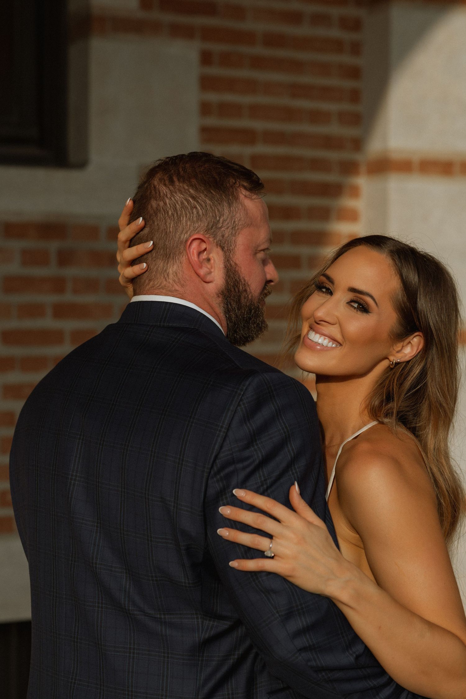 A romantic embrace between newlyweds sharing a joyful moment against a brick wall.