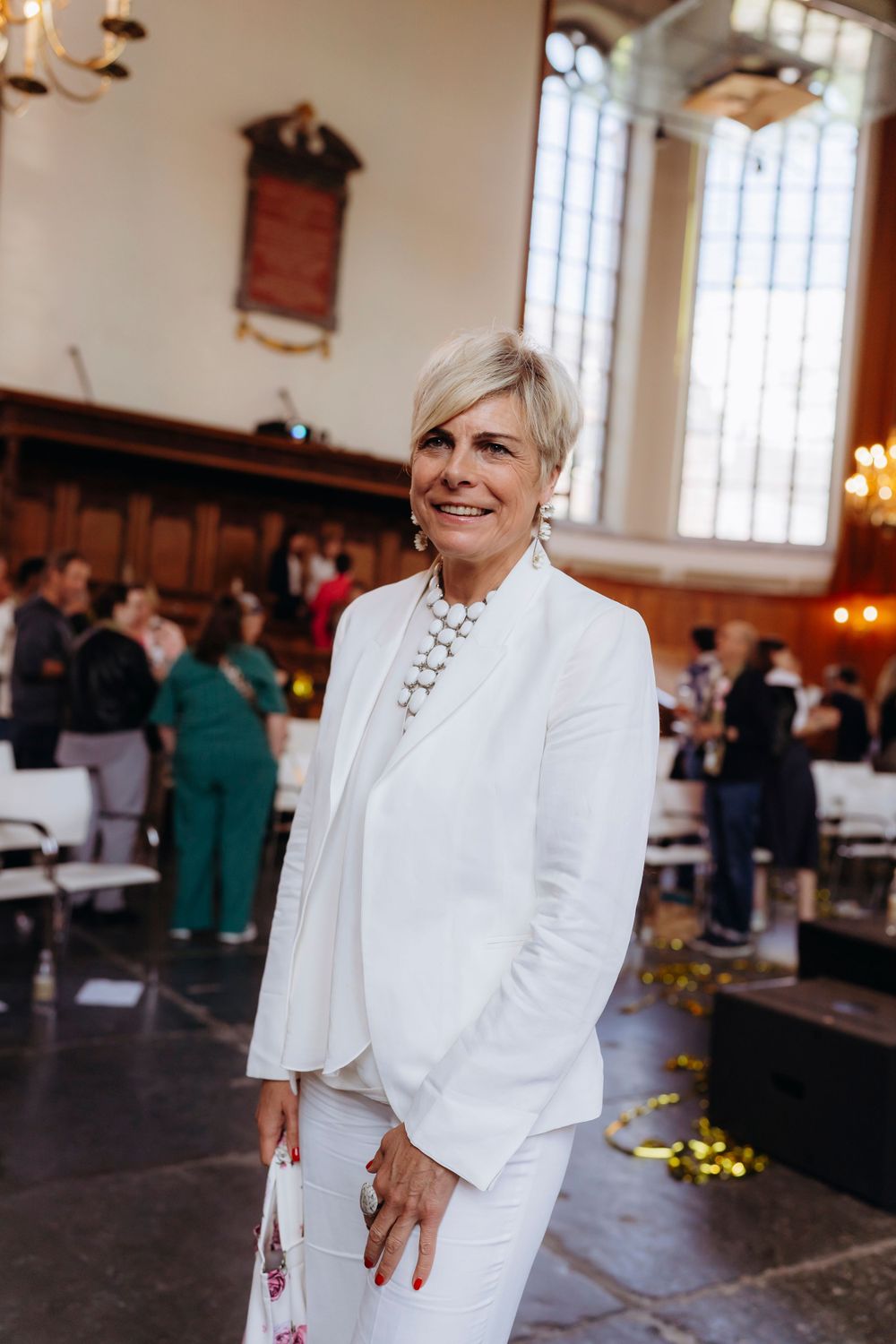 Person in elegant white blazer photographed in an indoor venue with warm lighting.