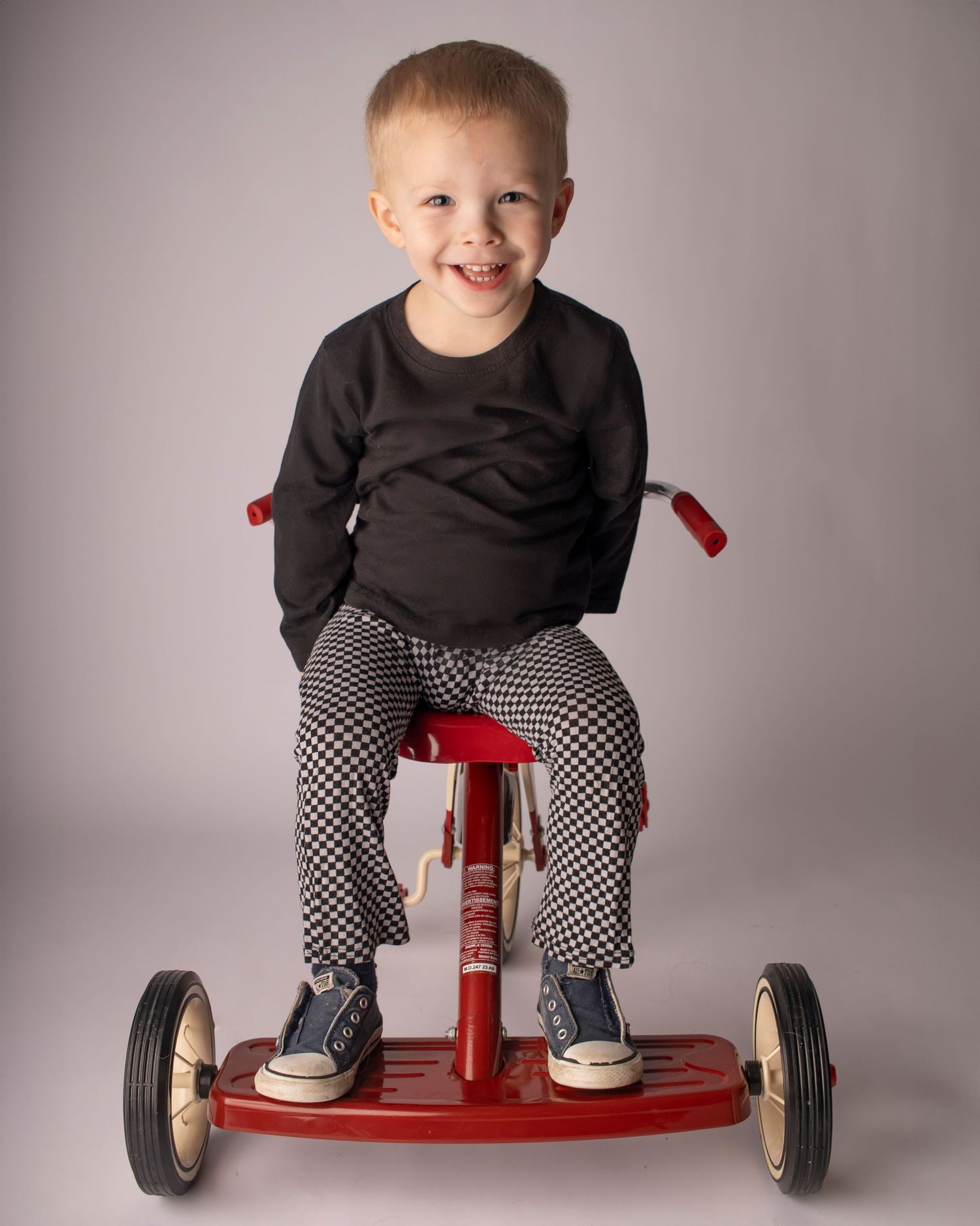 A young boy sits backwards on a tricycle with a wide smile