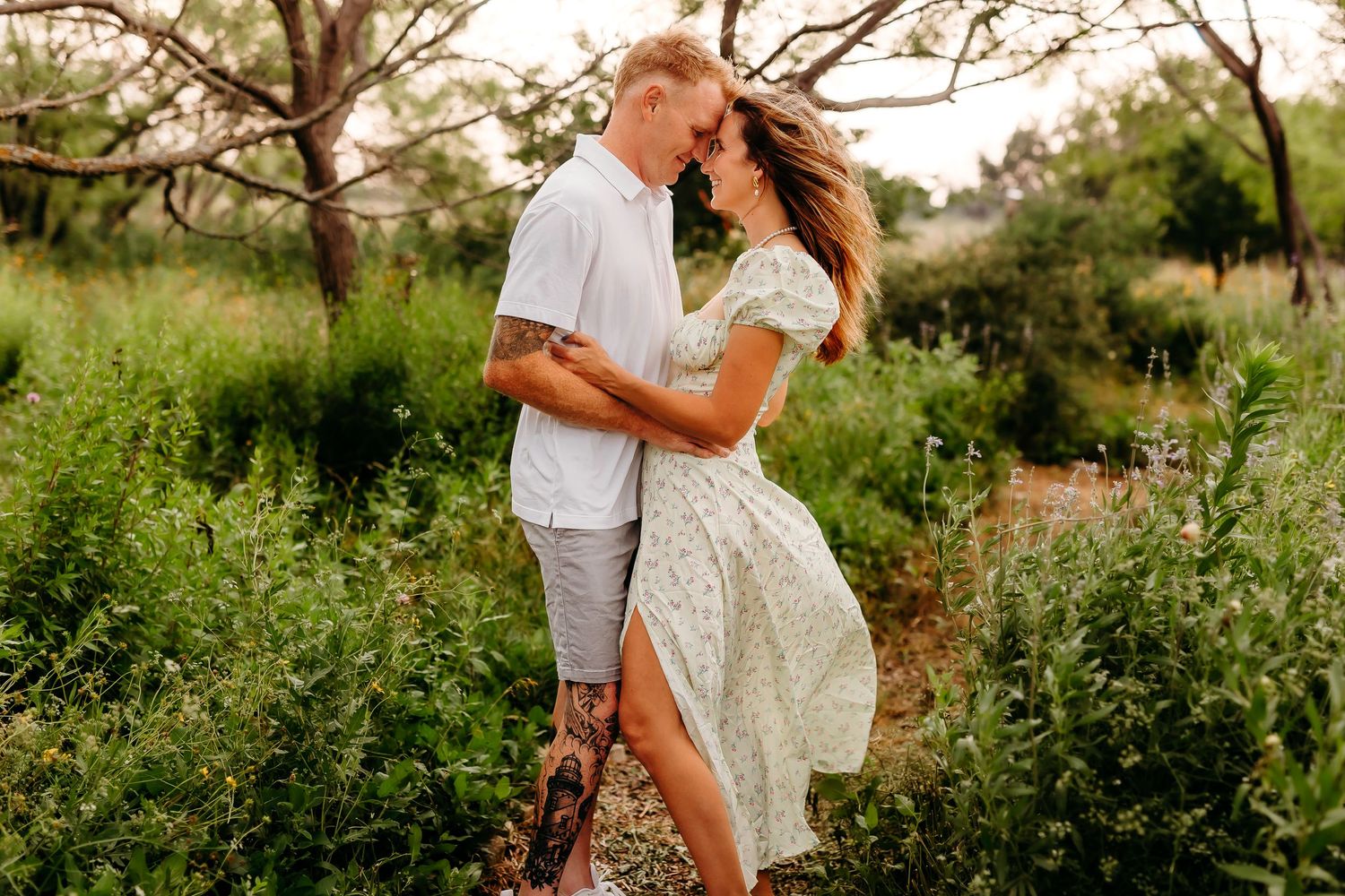 Romantic couple embracing in white summer attire amid blooming garden setting.