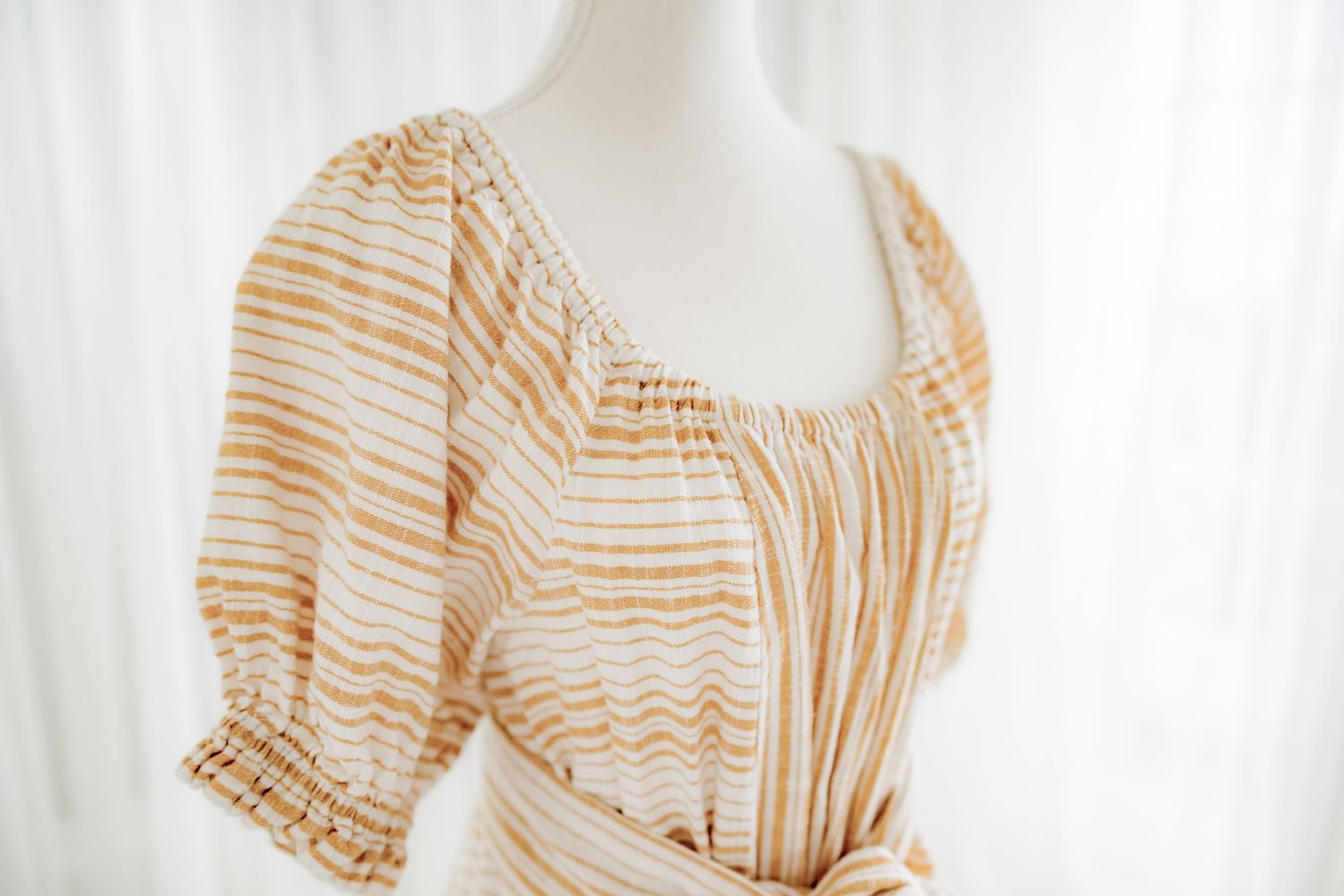 Detail shot of gathered neckline and puff sleeve on striped cotton dress.
