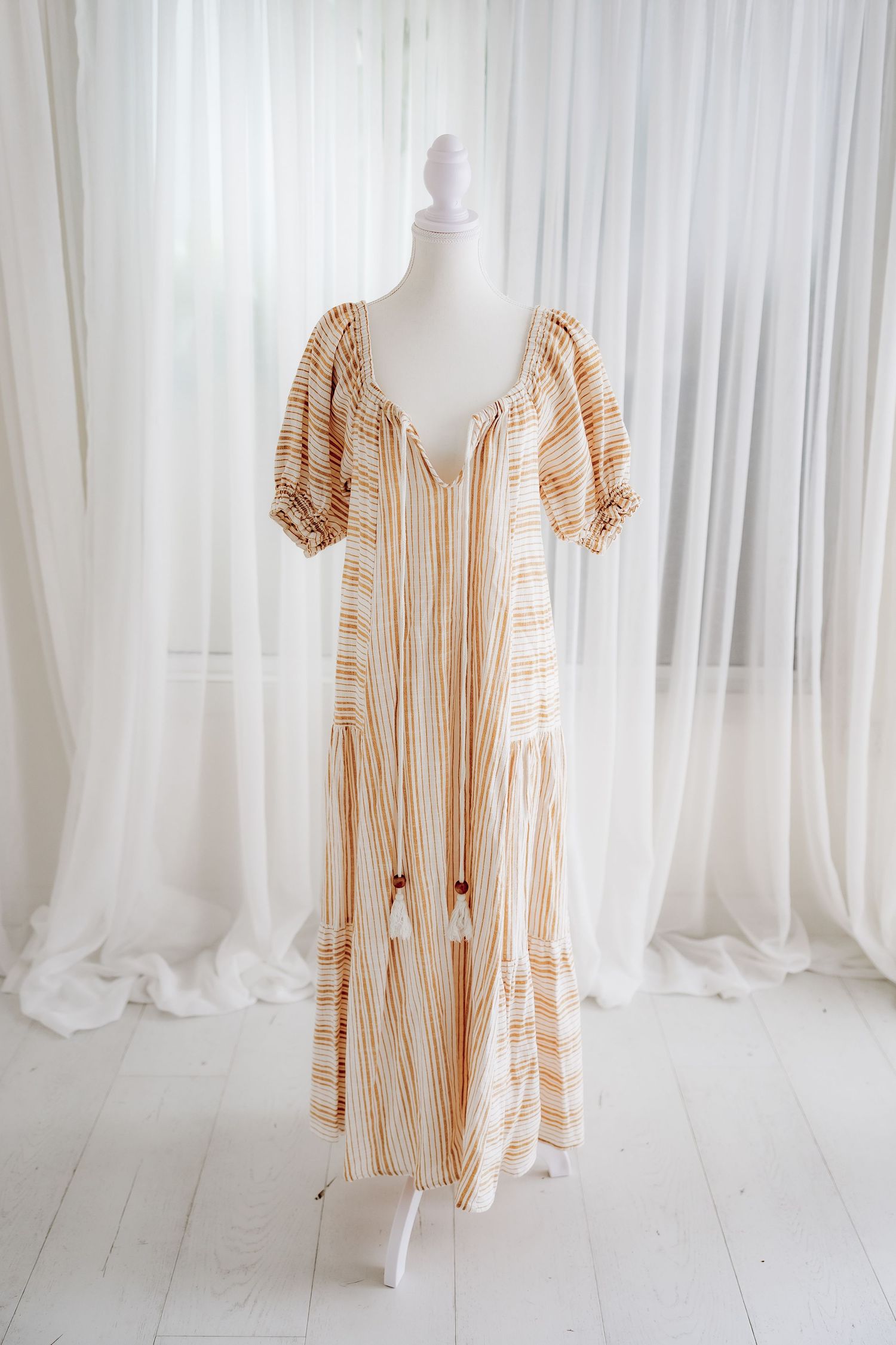 Beige and white striped maxi dress displayed on mannequin against white curtain backdrop.