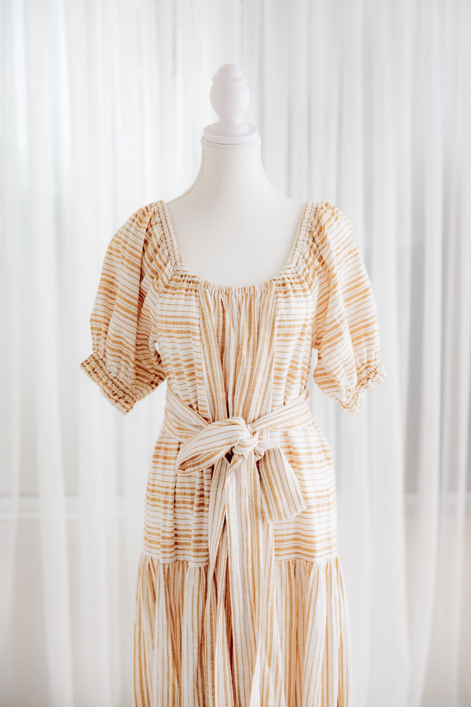 Vintage-style striped dress with puff sleeves and tie waist on white mannequin.