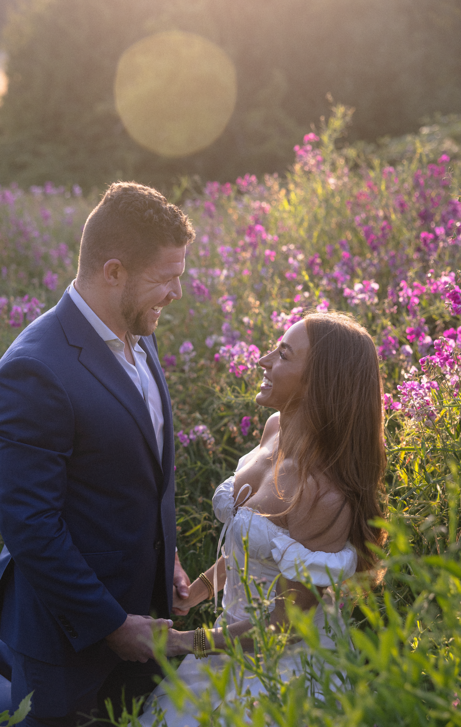 A romantic couple shares a joyful moment among blooming purple wildflowers at golden hour.