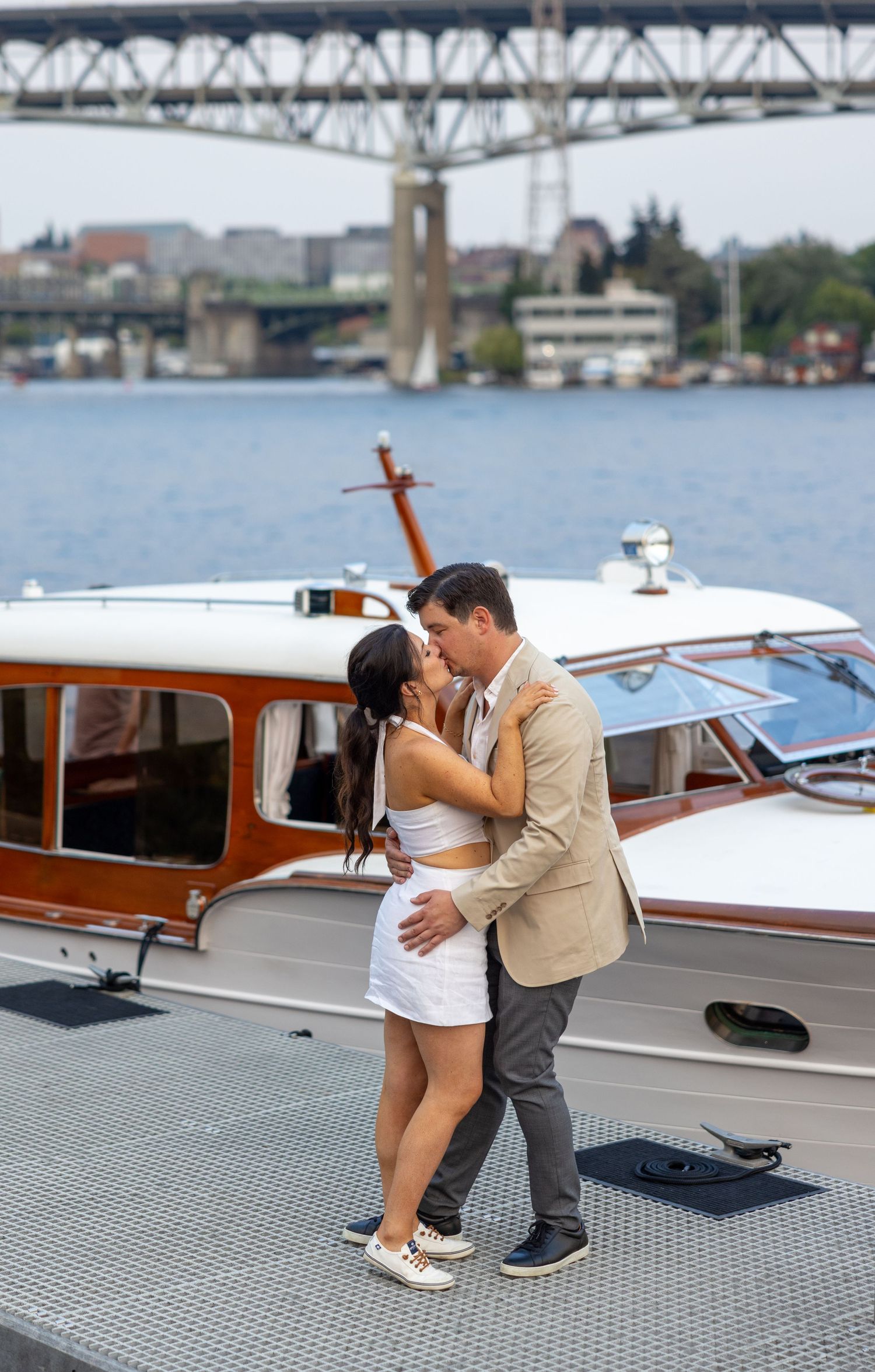 A romantic embrace on a boat dock with a classic wooden vessel in the background.