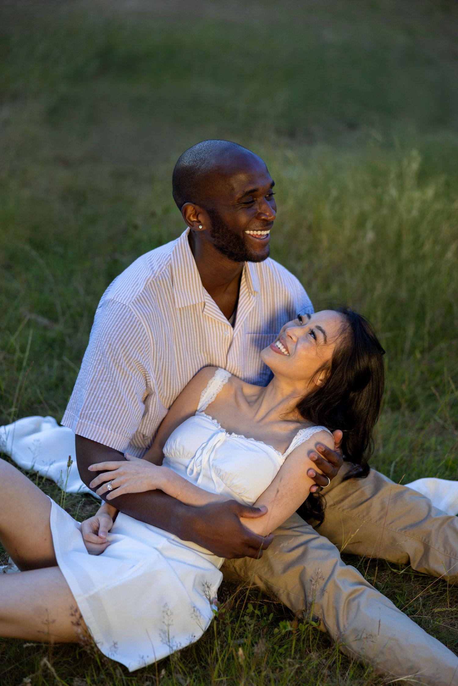 A couple shares a joyful moment together while relaxing on grass in warm sunlight.