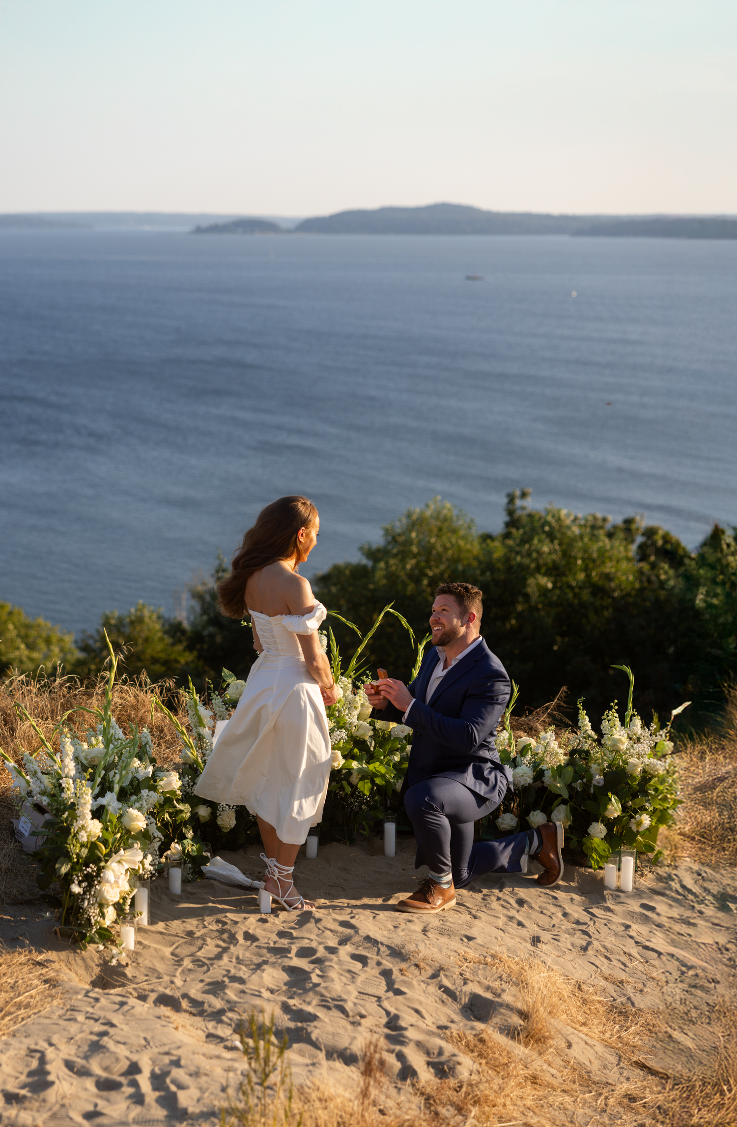 A beautiful outdoor beach wedding ceremony overlooking the ocean at sunset with floral arrangements and sandy terrain.