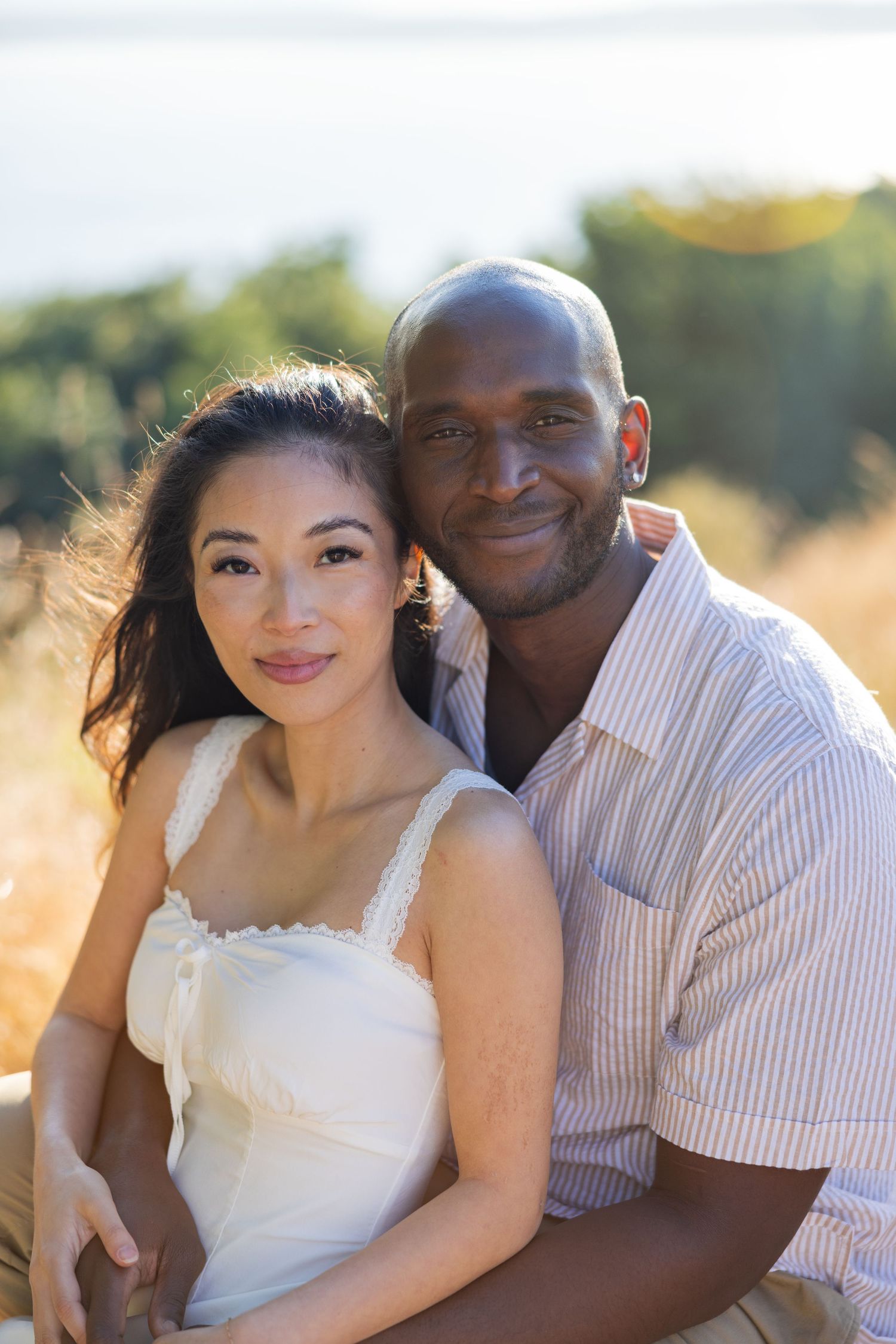 A couple poses together outdoors in a sunny field during a romantic photoshoot.