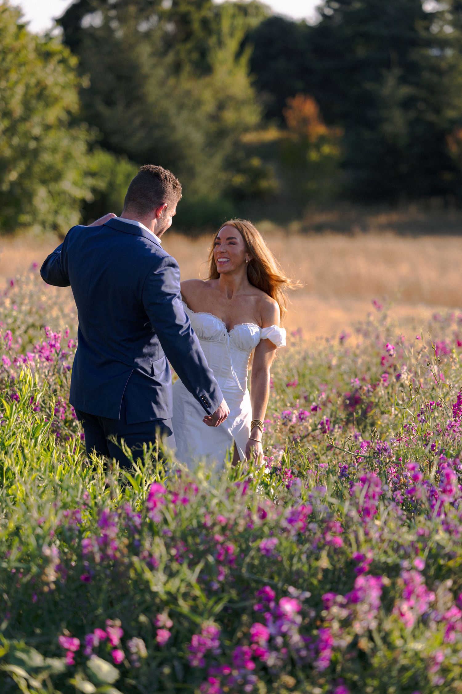 A couple shares a romantic moment in a field of vibrant purple wildflowers during golden hour.