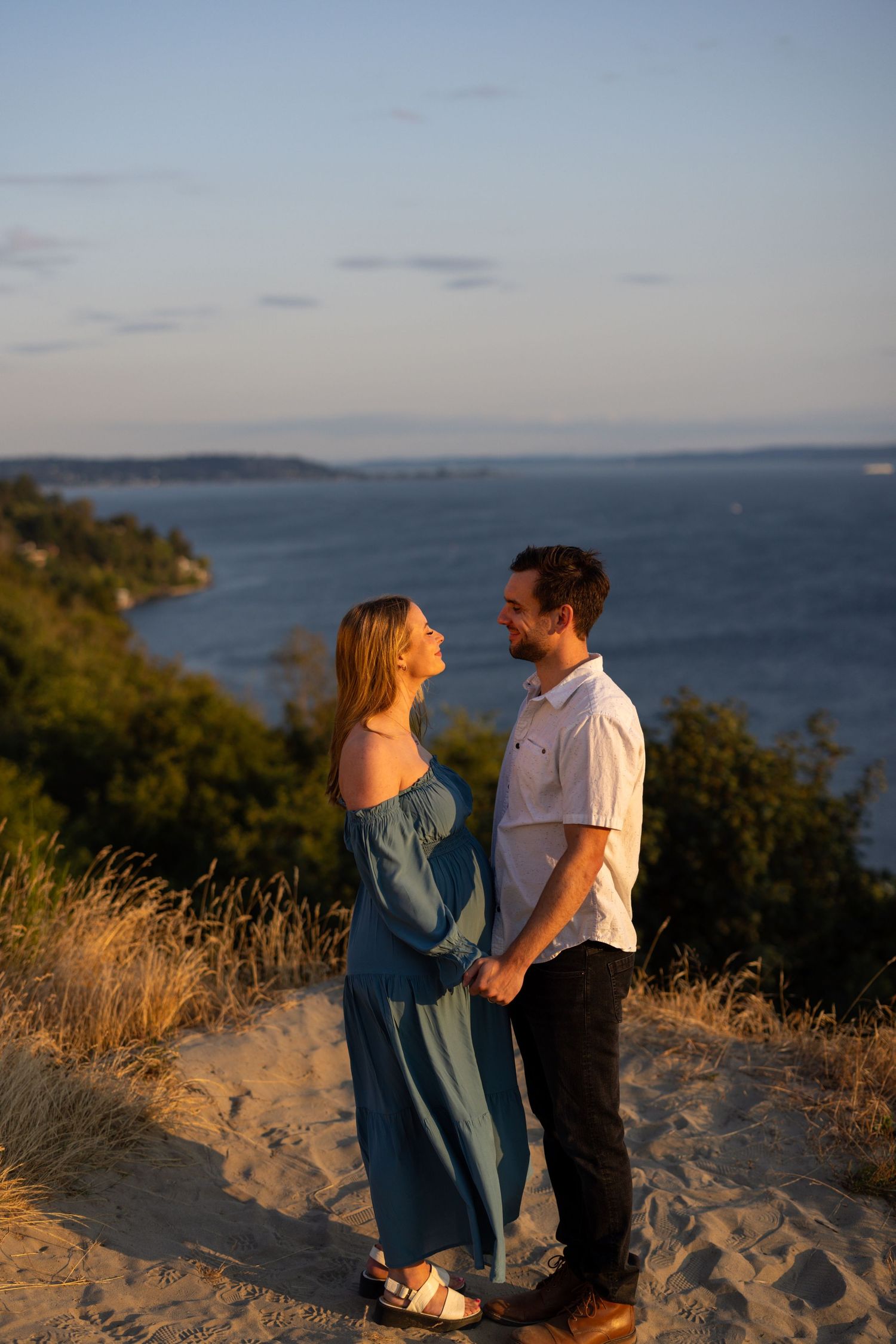 Couple sharing a romantic moment on a coastal cliff overlooking the ocean at golden hour.