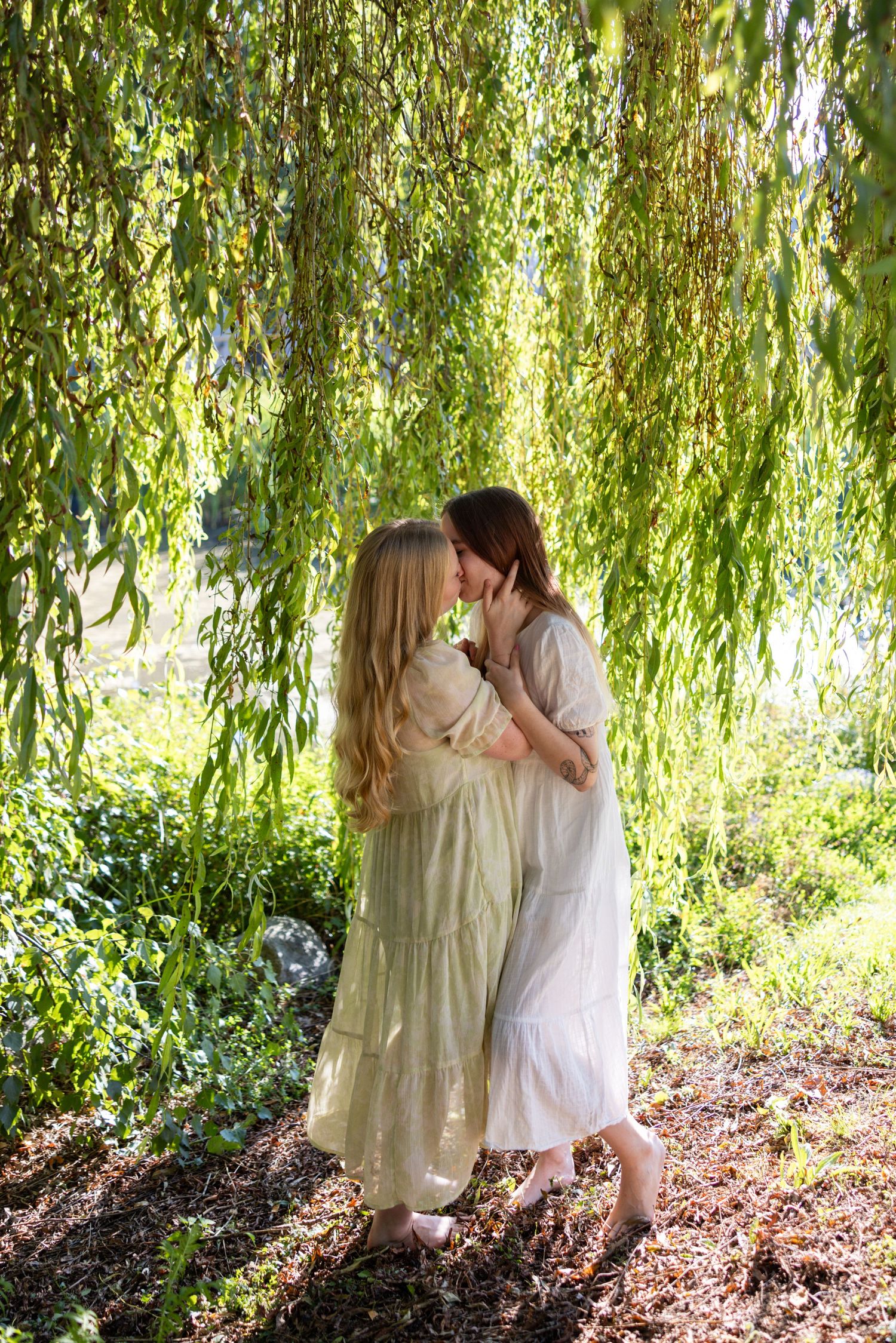 A romantic moment under drooping willow branches in a sunlit garden setting.