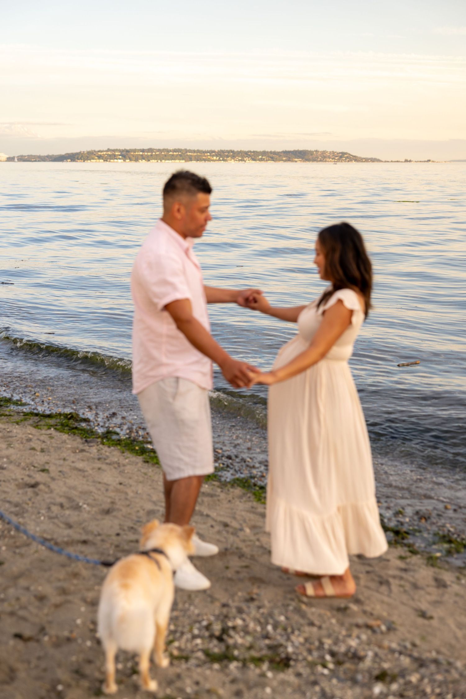Couple on a beach at sunset with their dog enjoying a peaceful moment by the water.