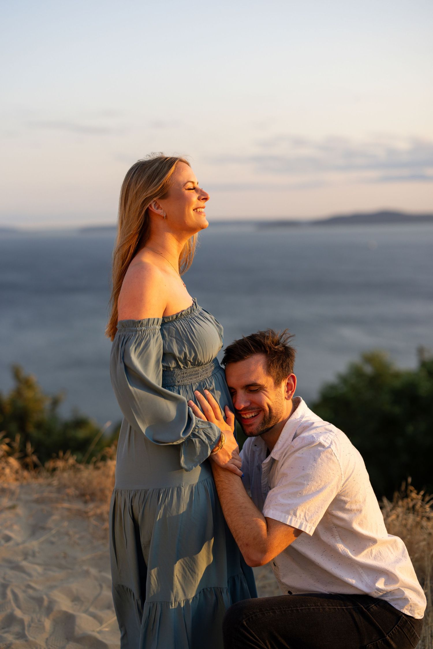 Sweet moment captured between couple on hilltop with ocean vista in background during sunset.
