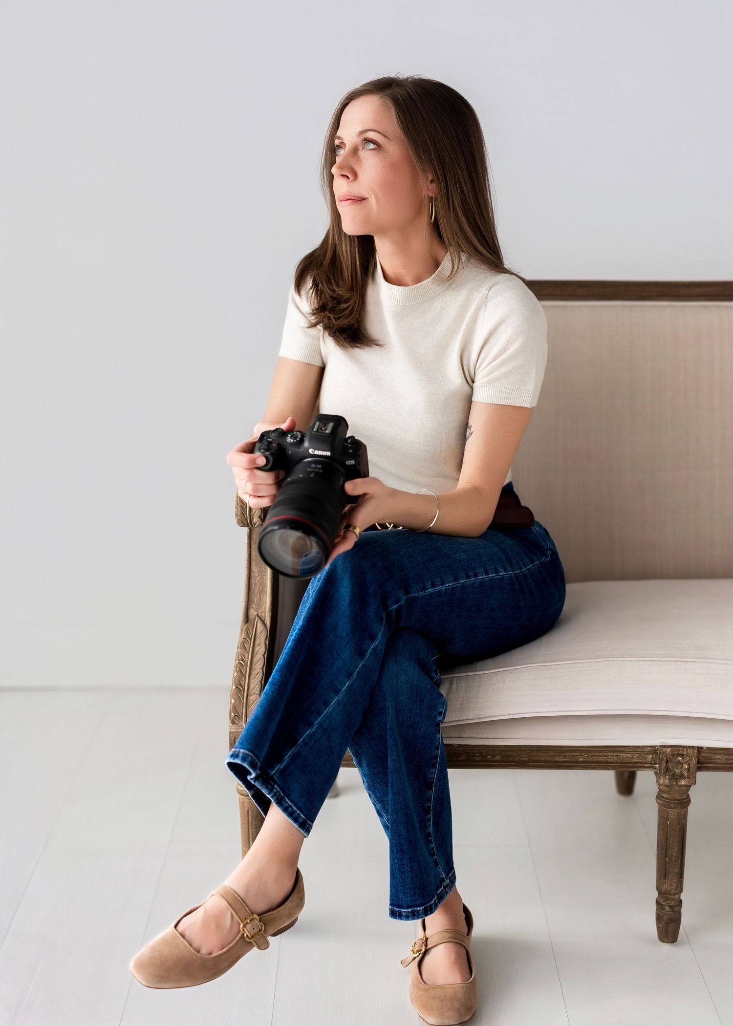 Professional photographer in denim jacket and navy dress poses with camera.