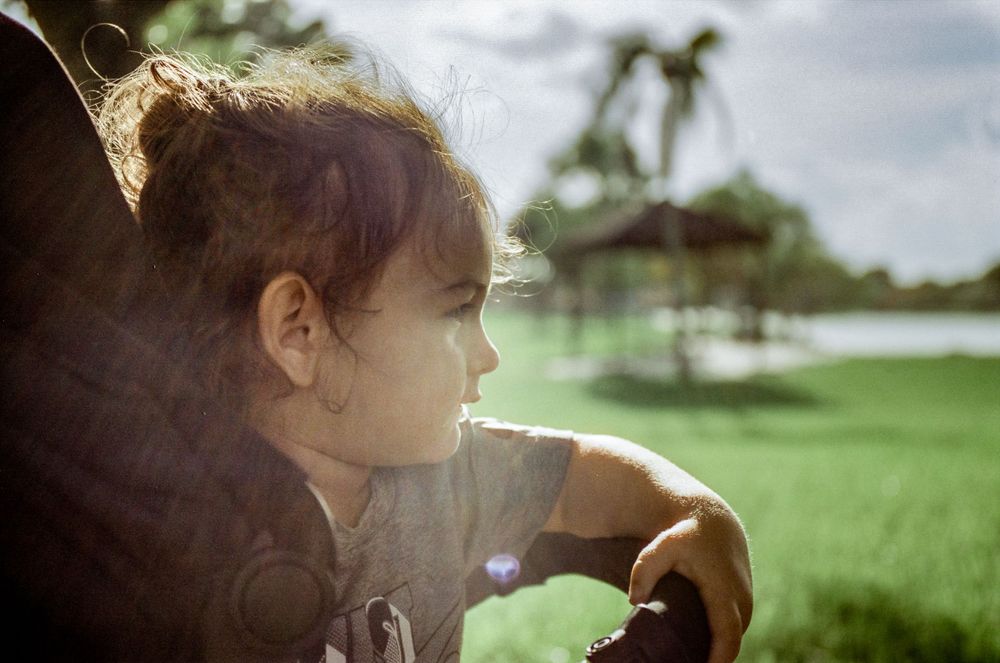 Side profile of a child looking off into the distance in a sunlit outdoor setting.
