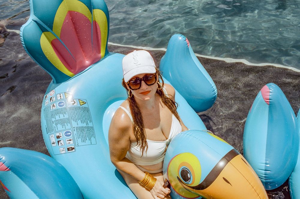 Someone relaxing on a colorful inflatable pool float shaped like a tropical bird.