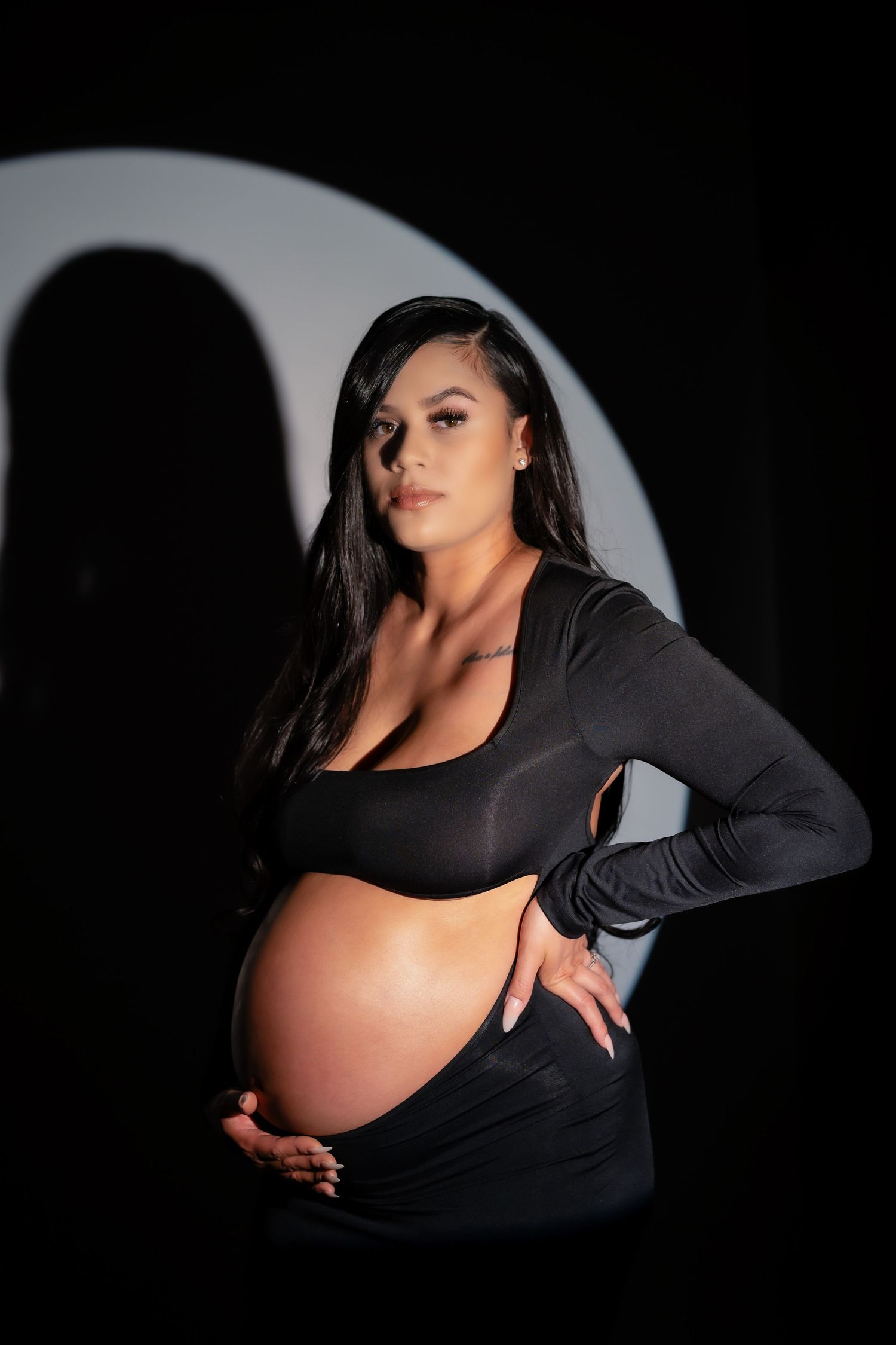 Artistic black and white maternity photos with dramatic lighting showcase a pregnancy silhouette in dark clothing.