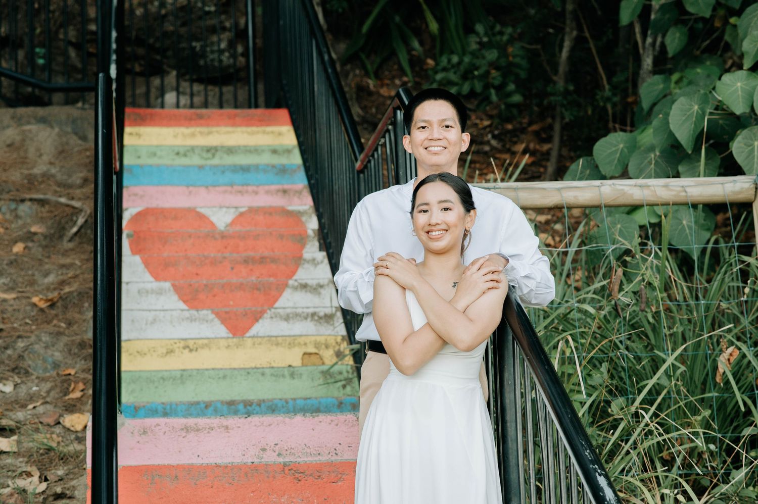 A couple embraces on colorful rainbow painted stairs with a heart design in a garden setting.