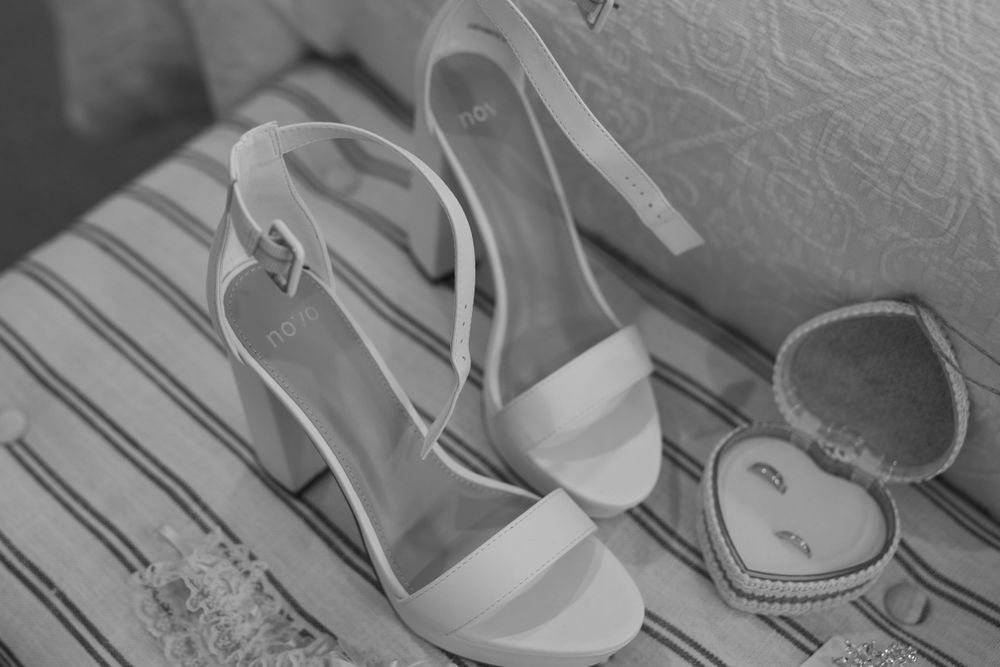 White wedding heels and a ring box arranged on a textured surface in black and white.