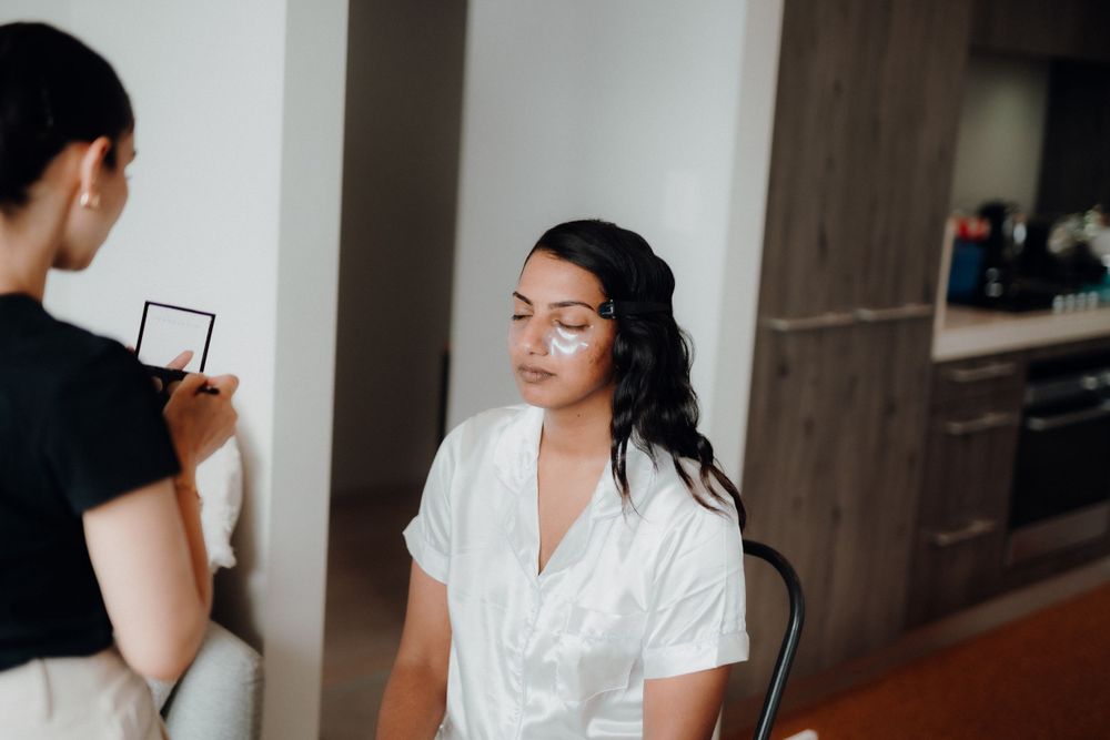 A makeup artist preparing to apply cosmetics on a client in a bright room.