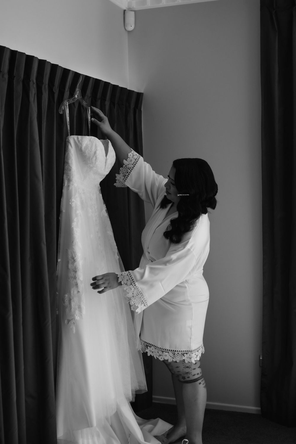 Black and white photo of someone in a white robe examining a hanging wedding dress.