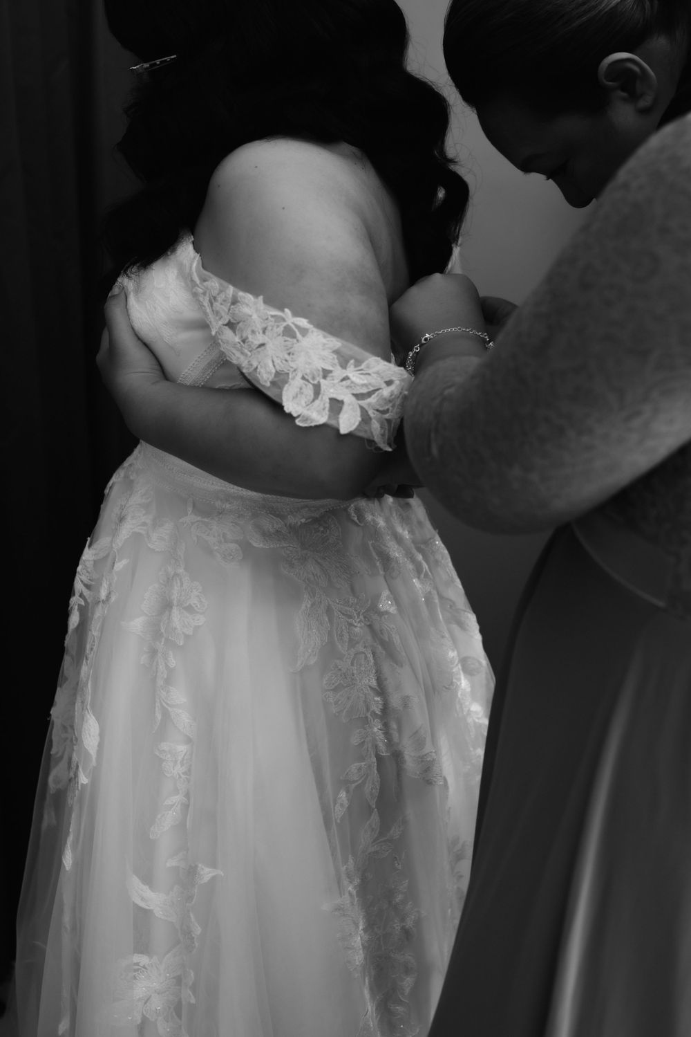 Black and white image showing detailed lace work being adjusted on a wedding dress.