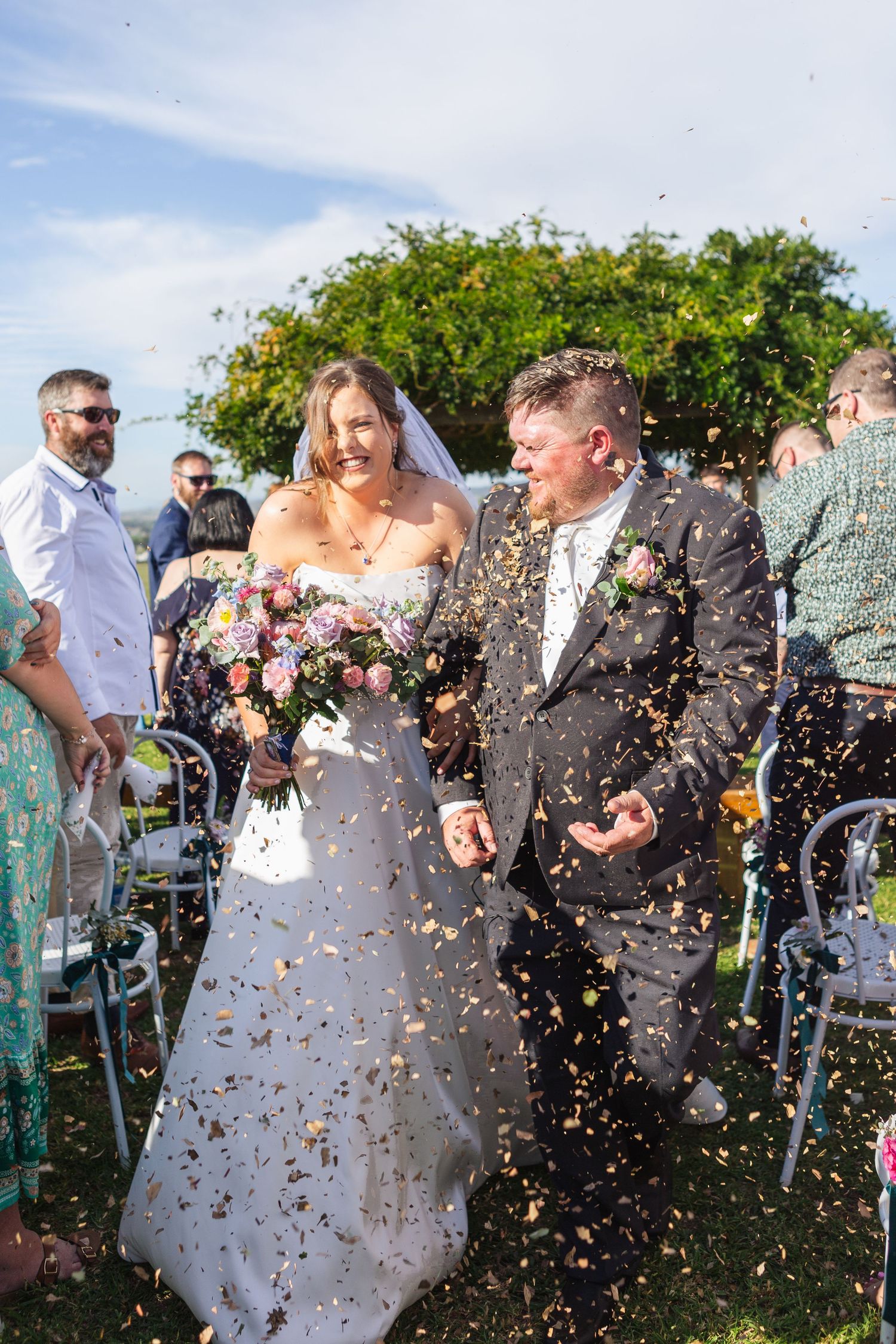 bride and groom walking down isle at their wedding holding hands while confetti falls down on them at Two Rivers Winery Denman Wedding