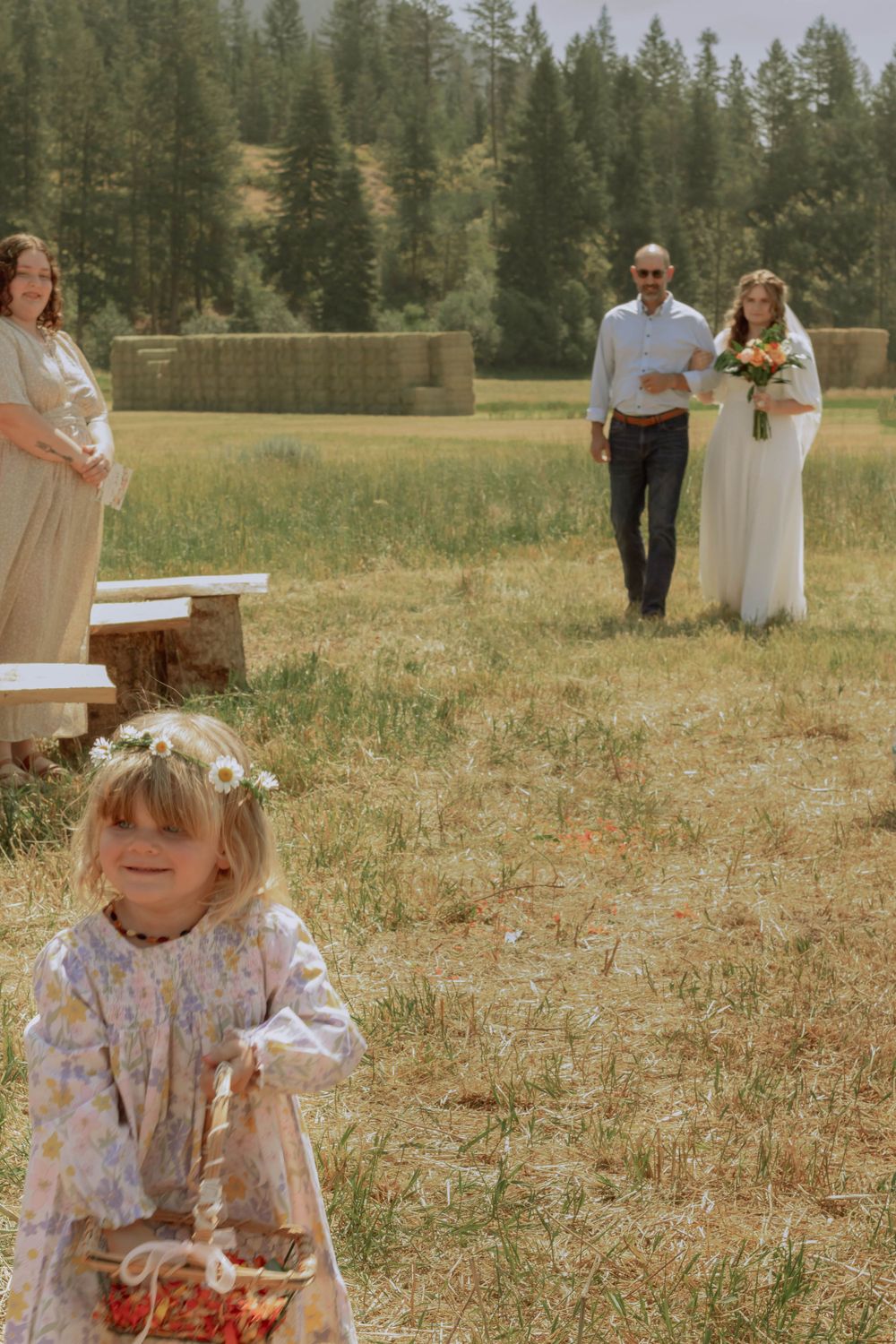 Toddler flower girl spreading rose petals in flower crown and pink dress in front of bride and her father walking down the aisle.