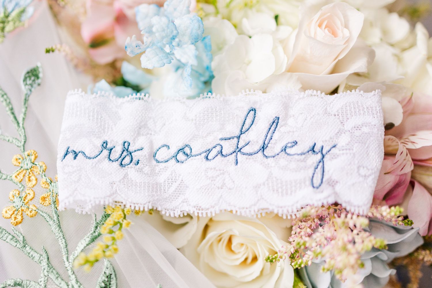 Custom embroidered 'Mrs. Coakley' name tag with blue lettering surrounded by pastel flowers.