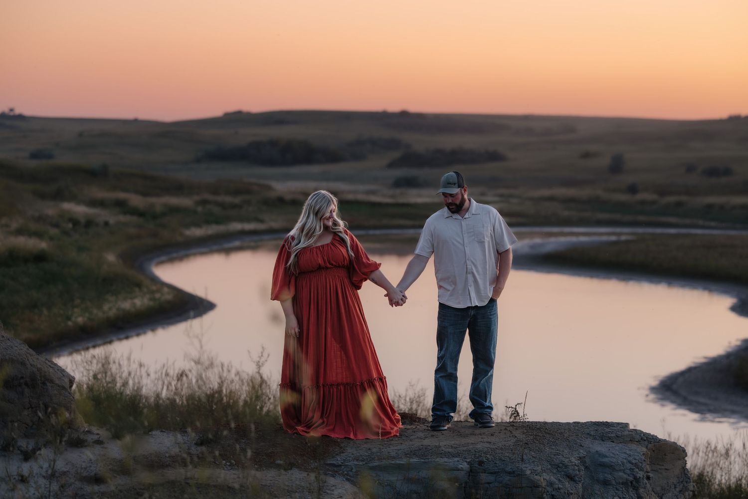 Engaged couple holding hands during golden hour overlooking Lake Sakakawea in boho client closet dress engagement photography Garrison, ND