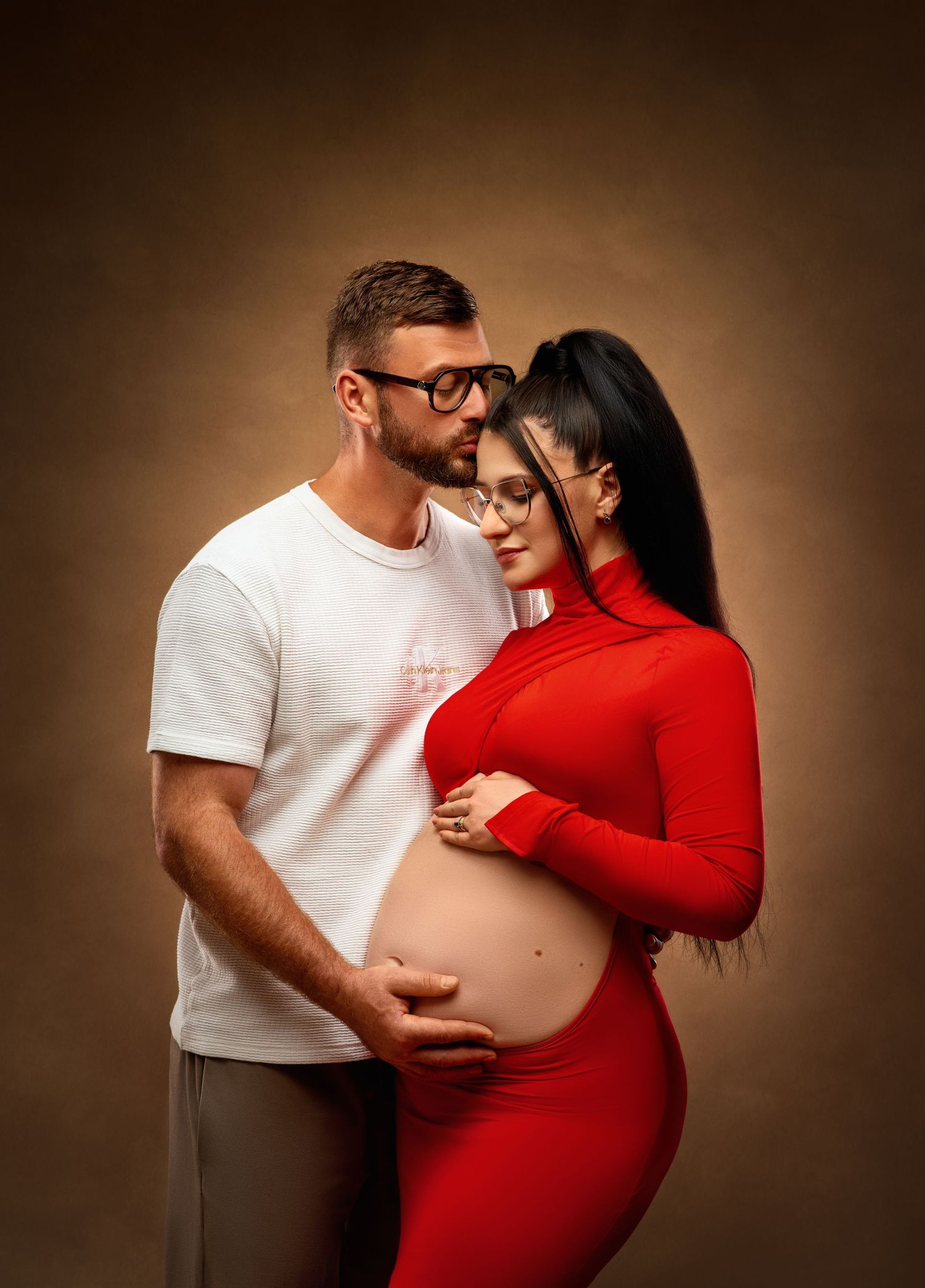 Black and white backlit silhouette of a couple in an intimate maternity pose against a white background.