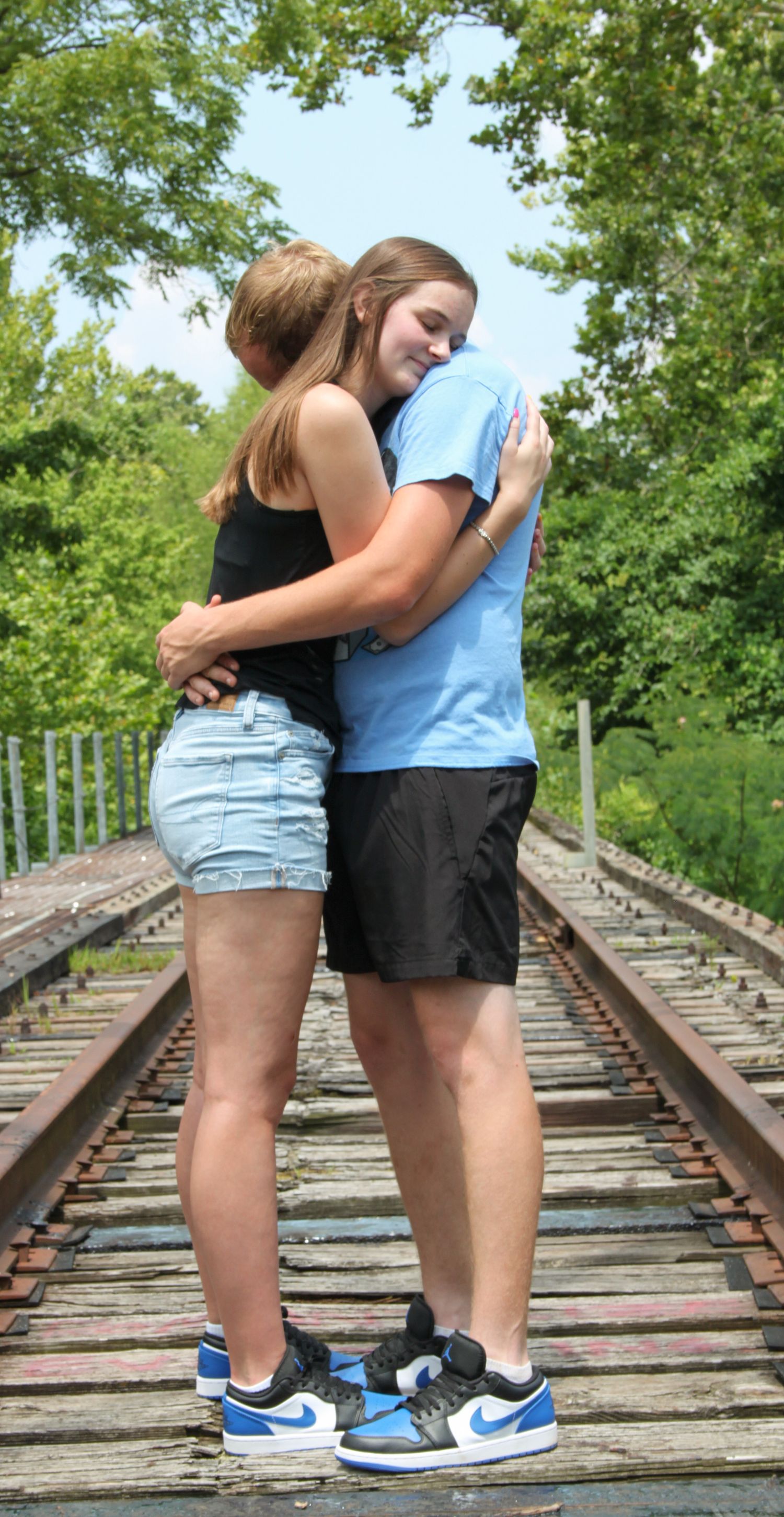 Boy and girl hugging on the trail tracks with trees behind them.