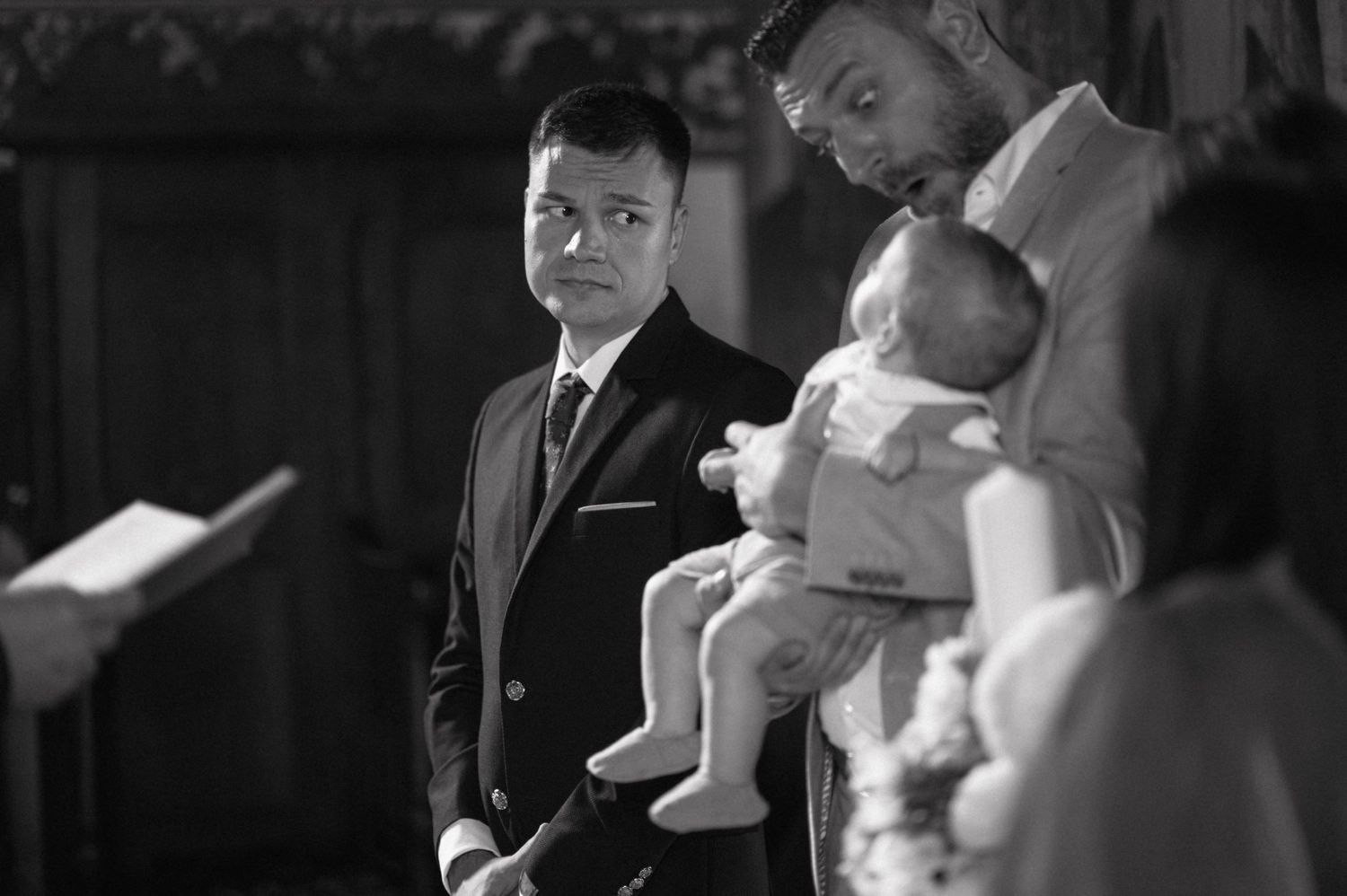 Black and white image of a solemn baptism ceremony in progress inside a church.