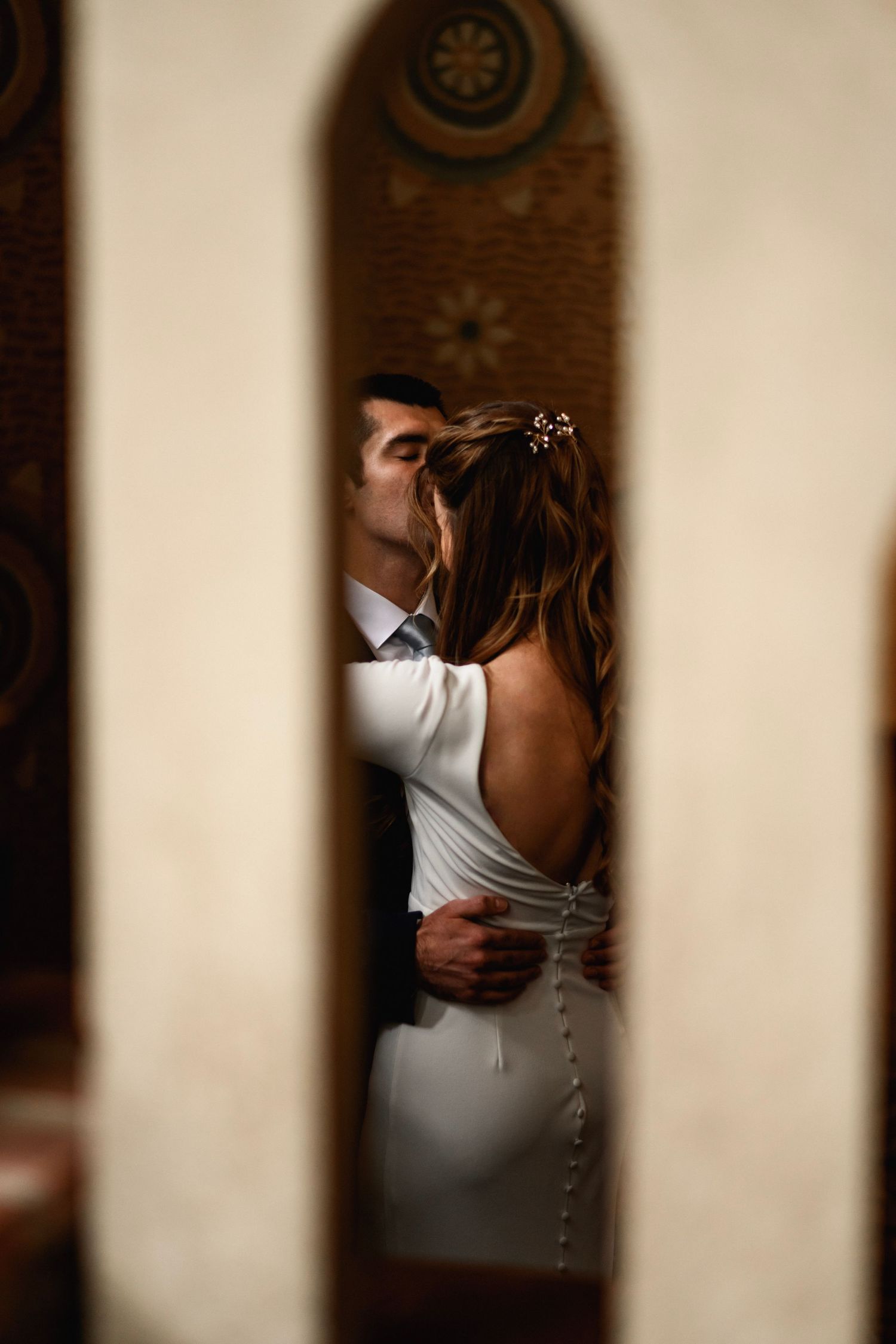 Romantic couple sharing a kiss, captured through a narrow archway with intricate decorative details.